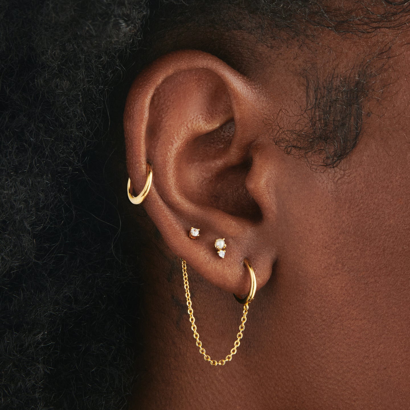 A gold small slim huggie with a connector chain with a 4mm open jump ring on ear. [hover] color:null|gold