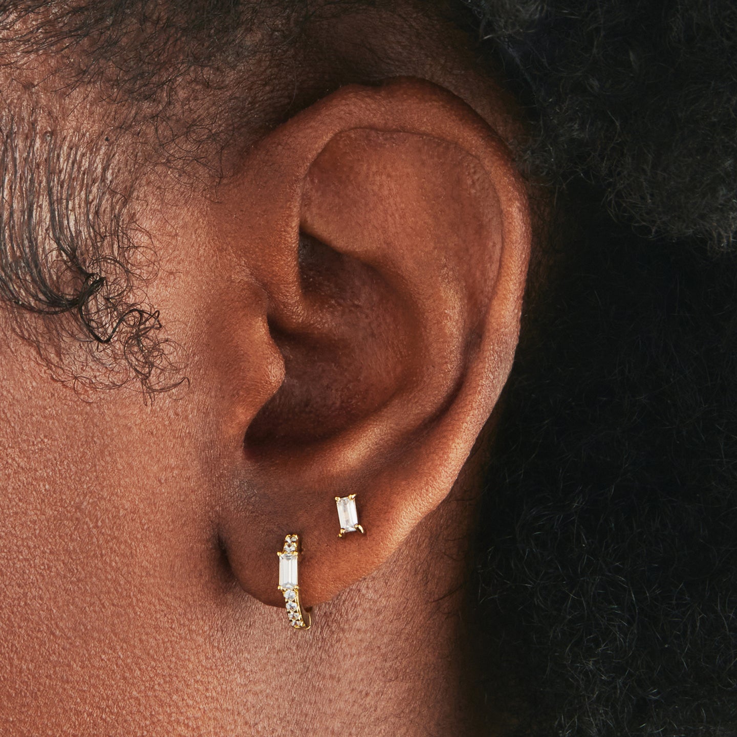 An image of gold/clear huggie with a clear accent baguette CZ stone on ear. [hover] color:null|gold/clear