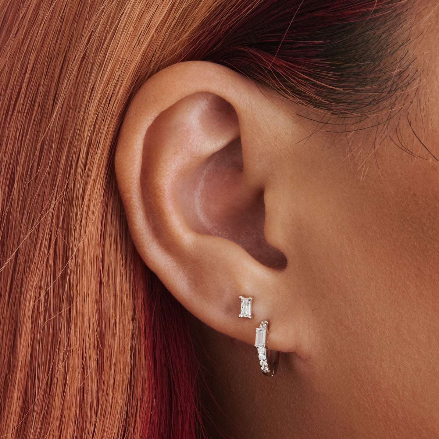An image of a silver/clear huggie with a silver accent baguette CZ stone on ear. [hover] color:null|silver/clear