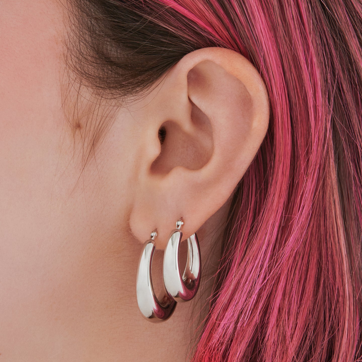 This is a silver, medium-sized, oval crescent shaped hoop on ear. [hover] color:null|silver