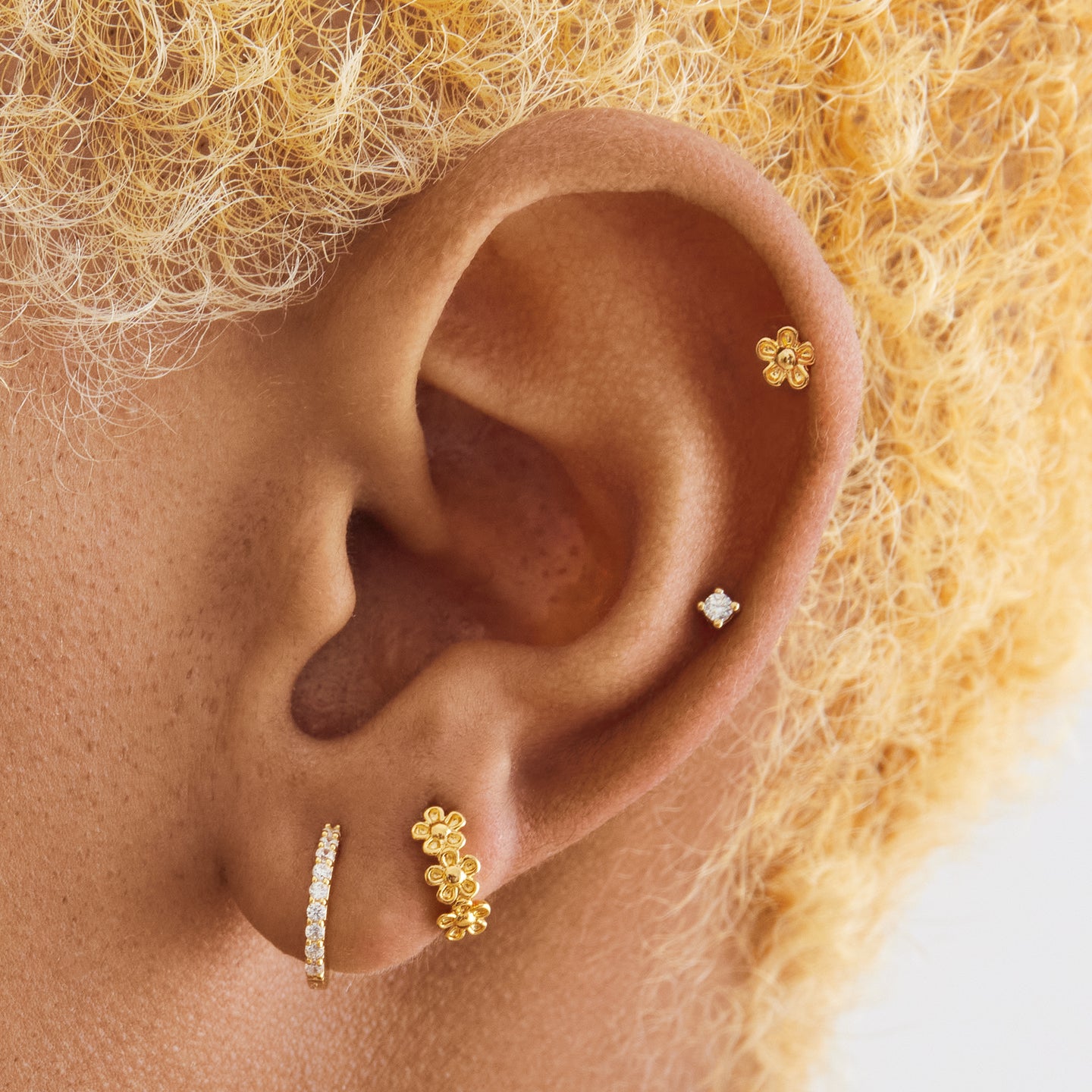 This is three small gold daisy-shaped flowers on a micro huggie on ear [hover] color:null|gold