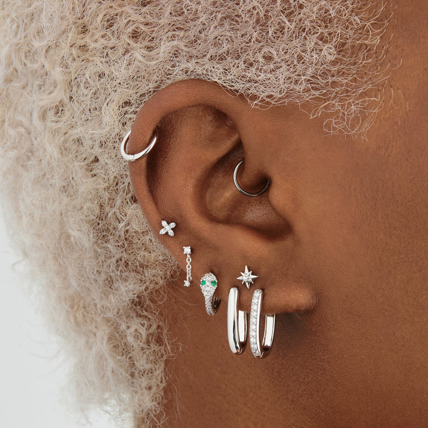 Silver pave gem lined serpent shaped huggie with green CZ eyes on ear [hover] color:null|silver/clear