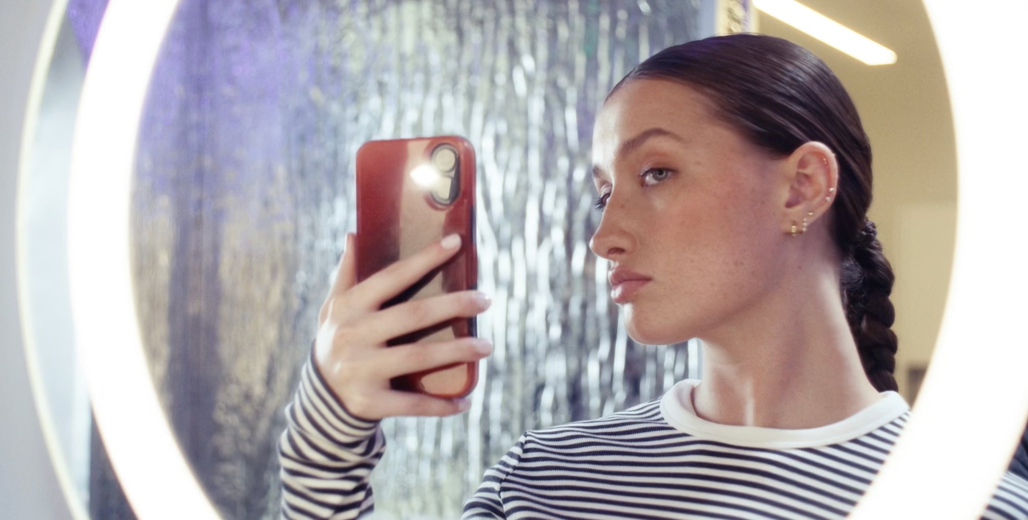 Woman taking a mirror selfie of her ear that has multiple piercings with a smartphone in a Studs store.
