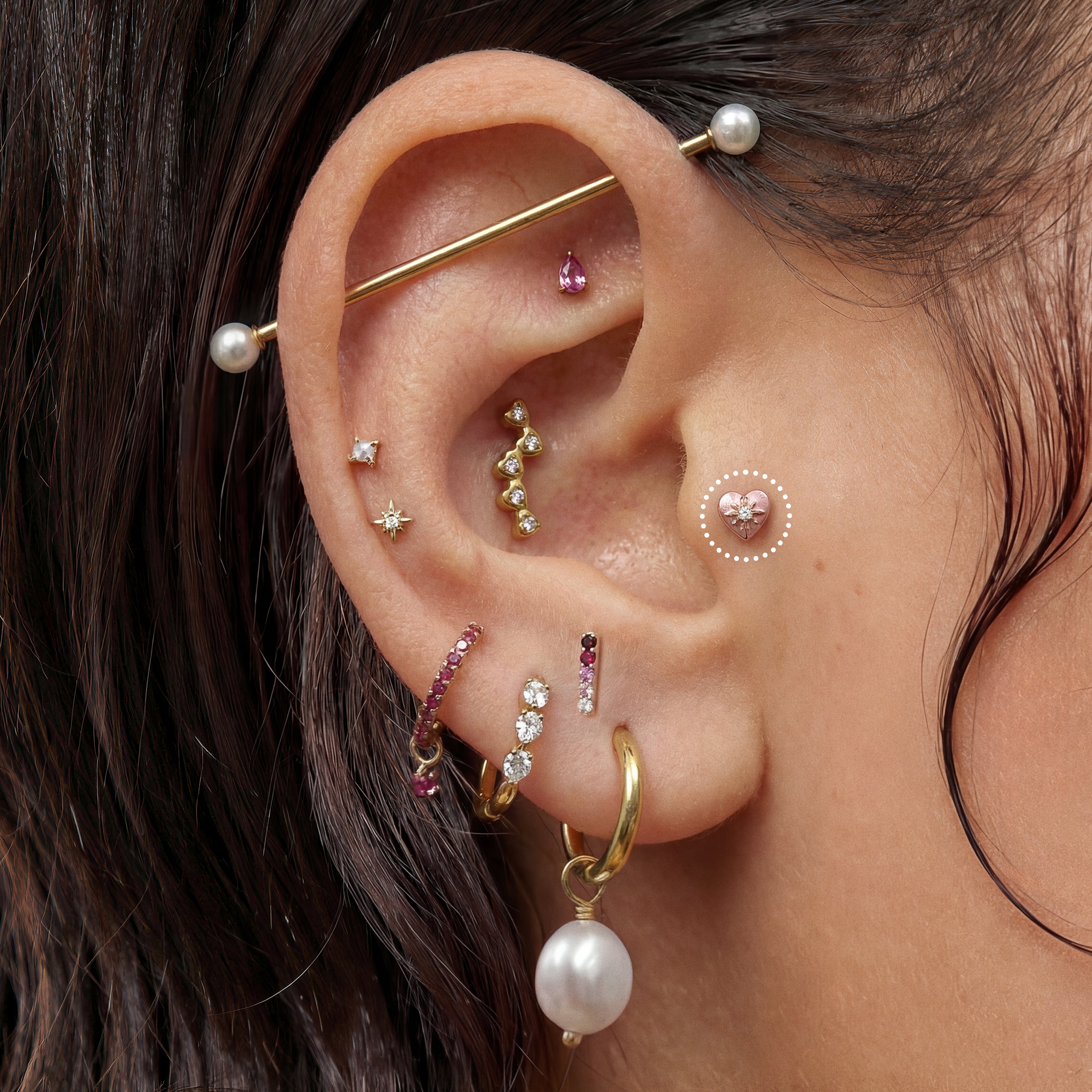 Close-up of an ear with multiple gold and pearl earrings featuring a pink twinkle heart flatback stud 