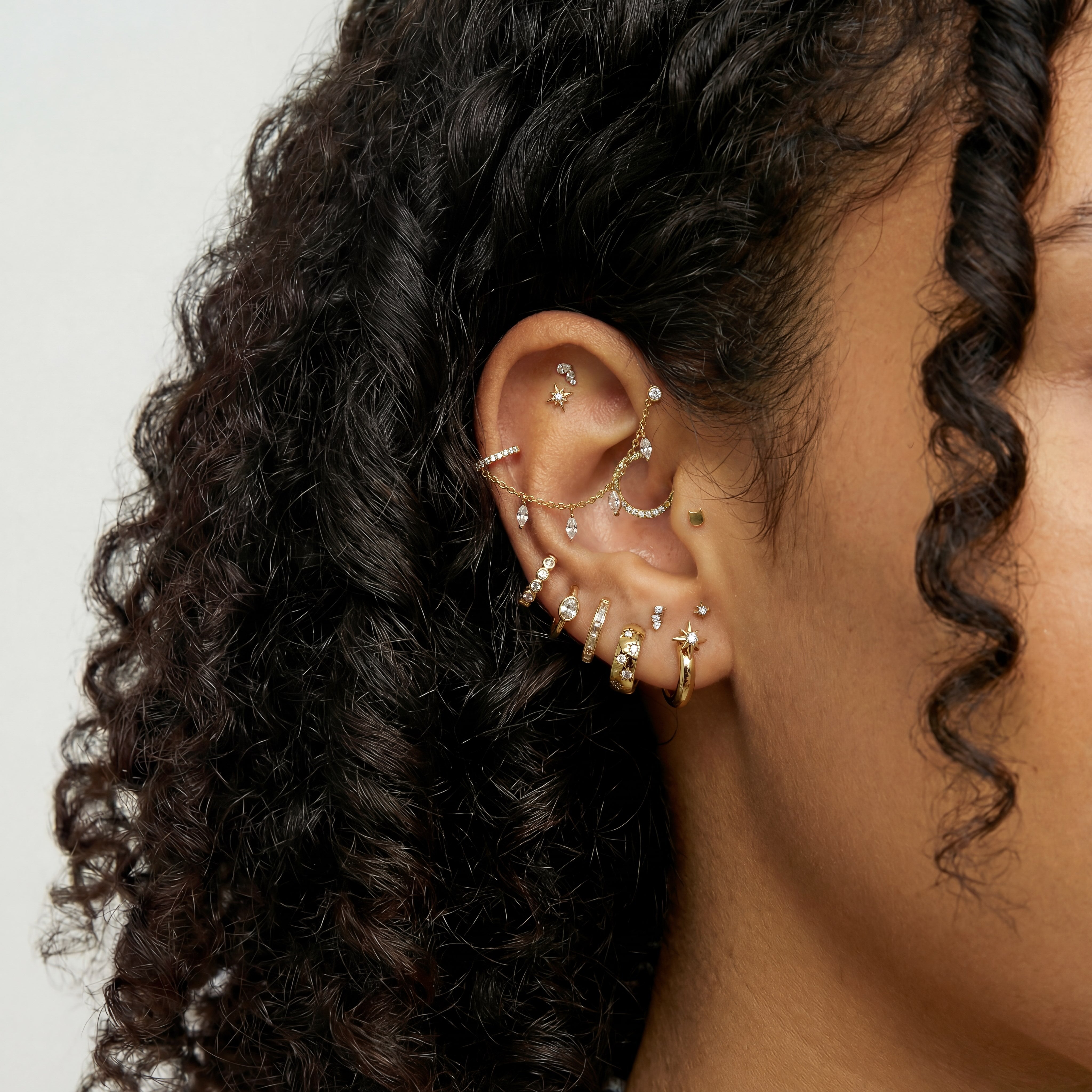 Close-up of an ear with multiple gold earrings including a marquise dangle chain