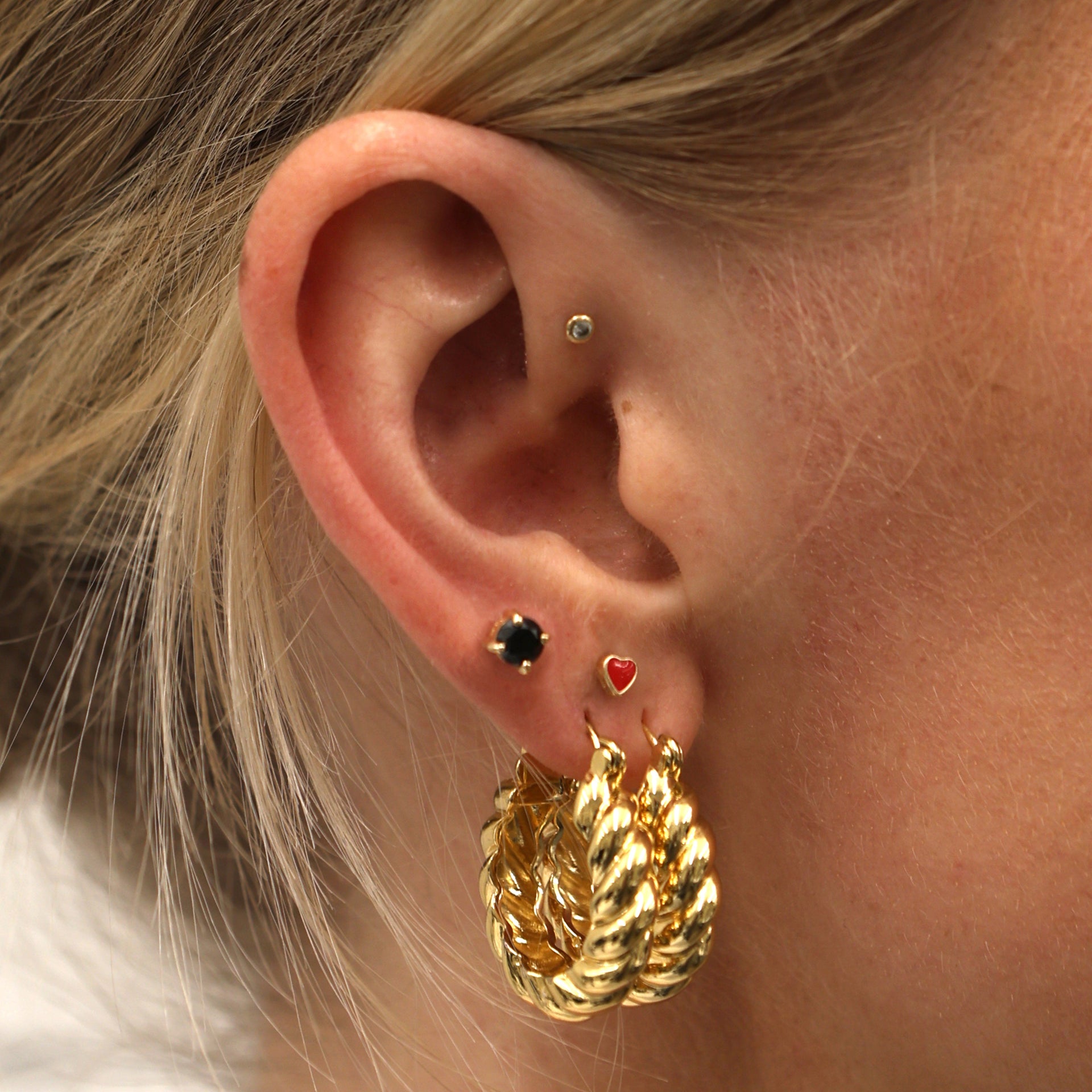 Close-up of an ear with two chunky gold hoops, a black cz flatback, and a red enamel heart flatback