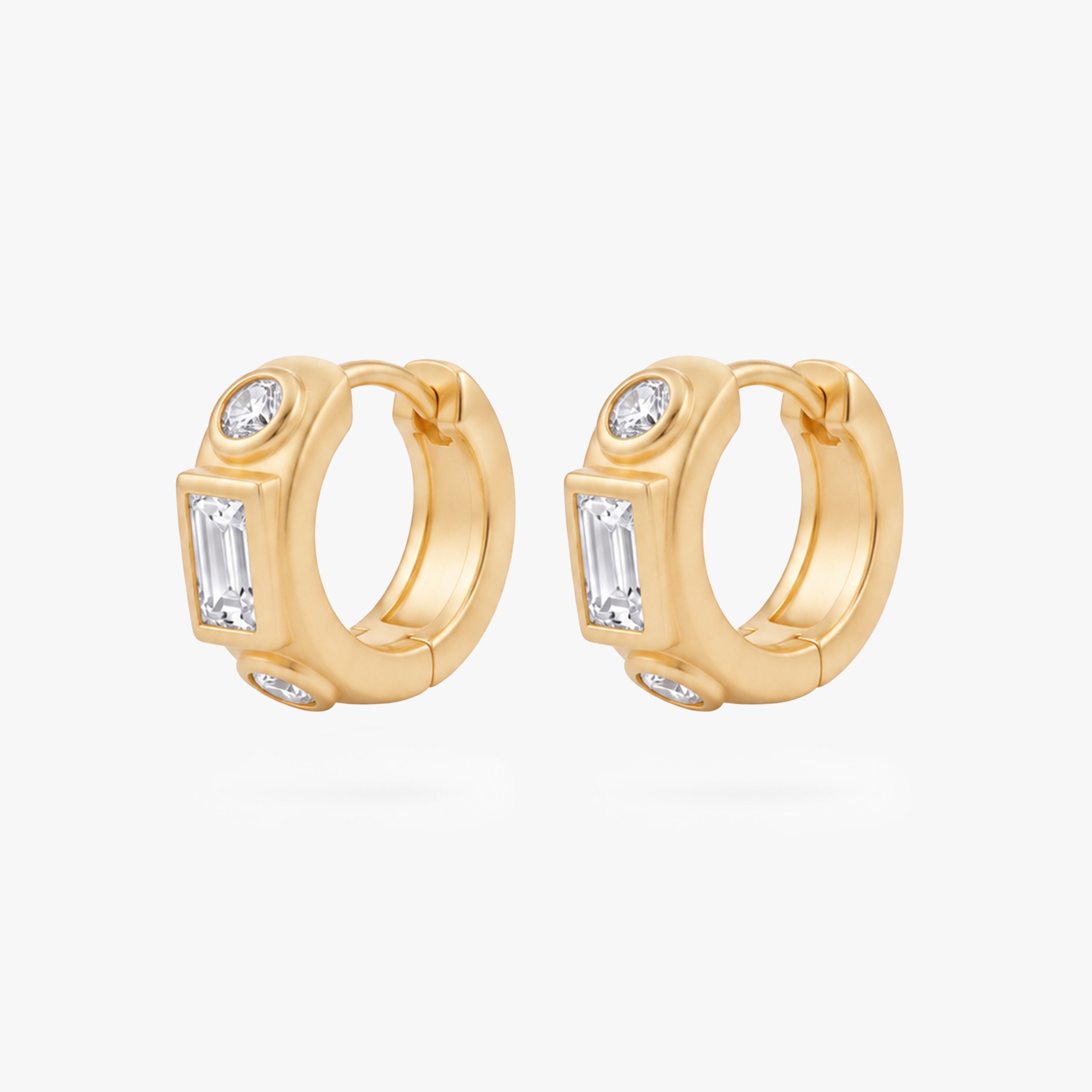 This image shows the front view of a pair of 14k gold plated huggies with three clear cz stones. One square in the middle and two circular stones on the outside. - Pair view