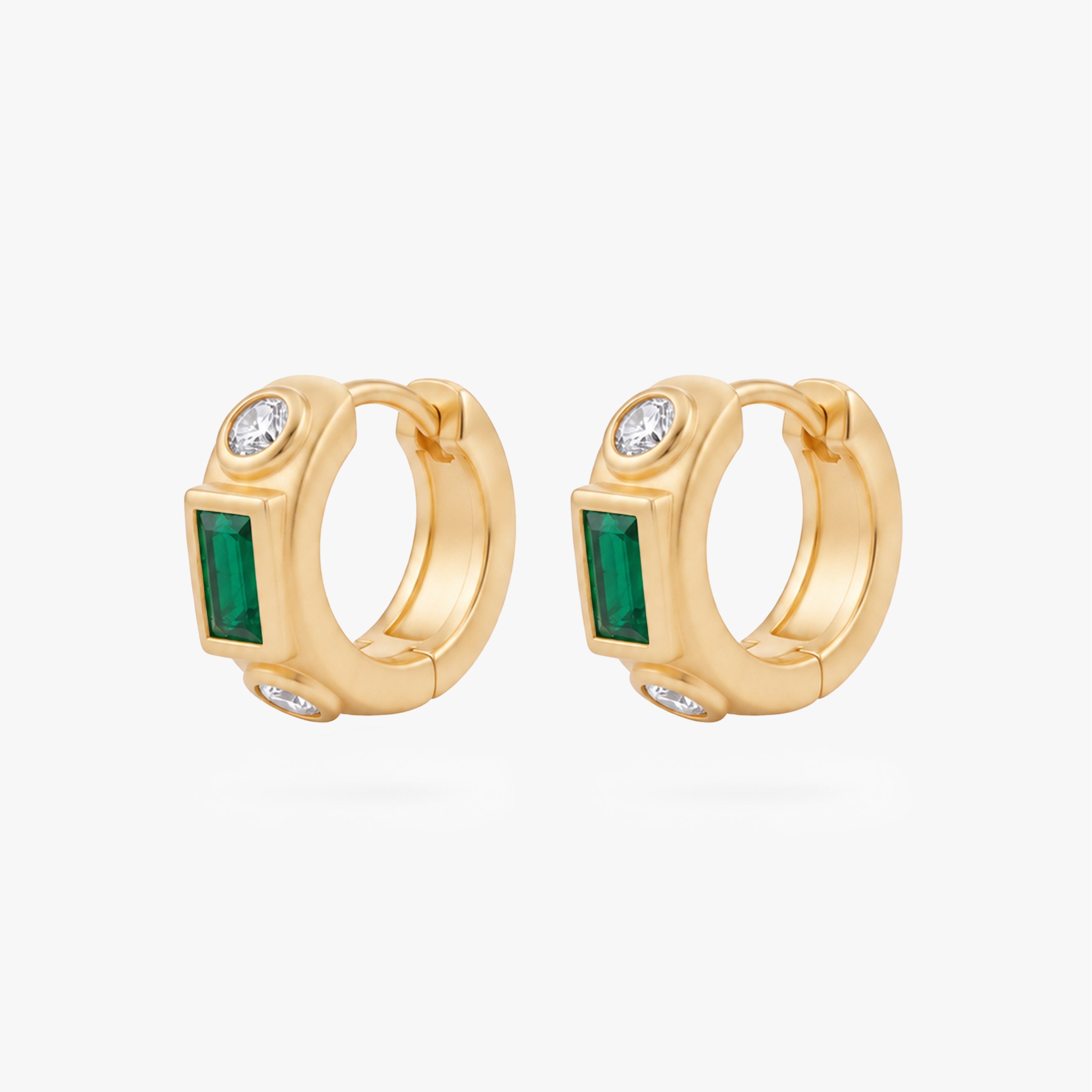 This image shows the front view of a  pair of 14k gold plated huggies with three cz stones. One green square in the middle and two clear circular stones on the outside. - Pair view