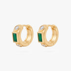 This image shows the front view of a  pair of 14k gold plated huggies with three cz stones. One green square in the middle and two clear circular stones on the outside.