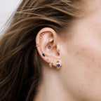 this image shows an ear with a 14k gold plated huggie with three blue circular cz stones