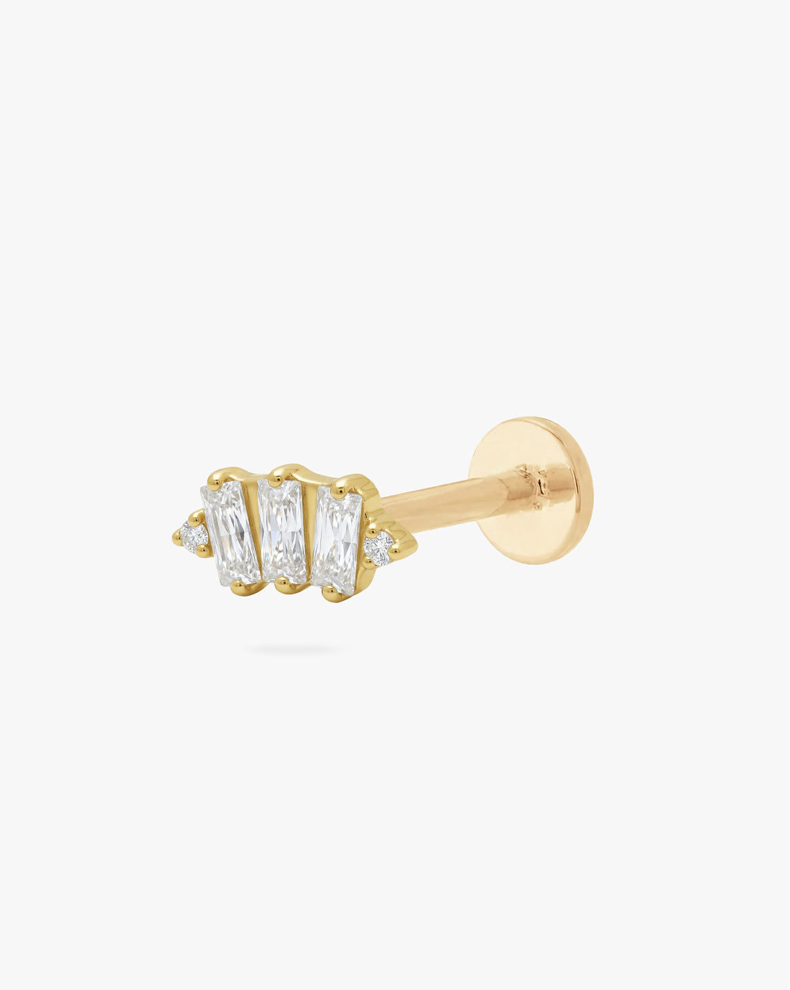 A gold post piercing stud featuring three baguette-cut clear crystals and small accent stones, shown on a plain light gray background.