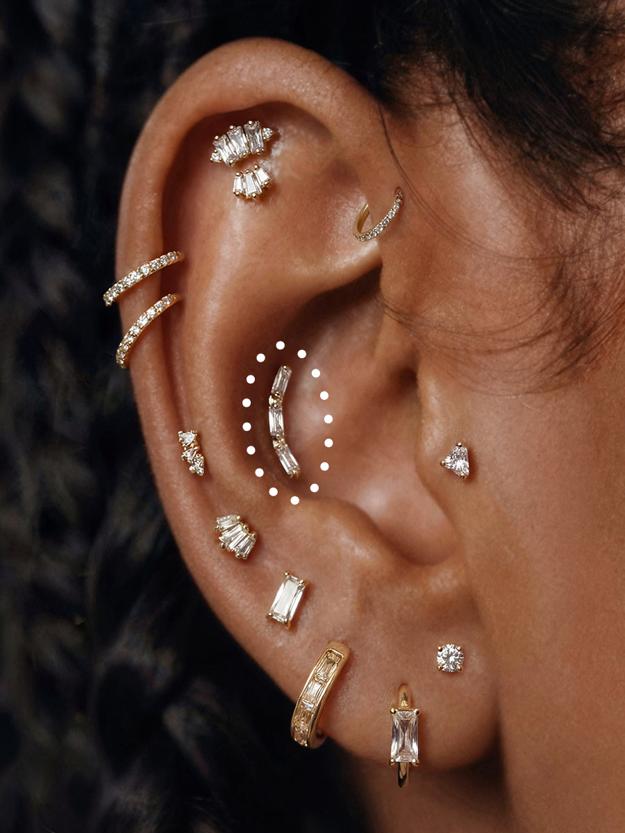 Close-up of a person's ear adorned with multiple gold and silver ear piercings and studs, including hoop, stud, and cartilage piercings.