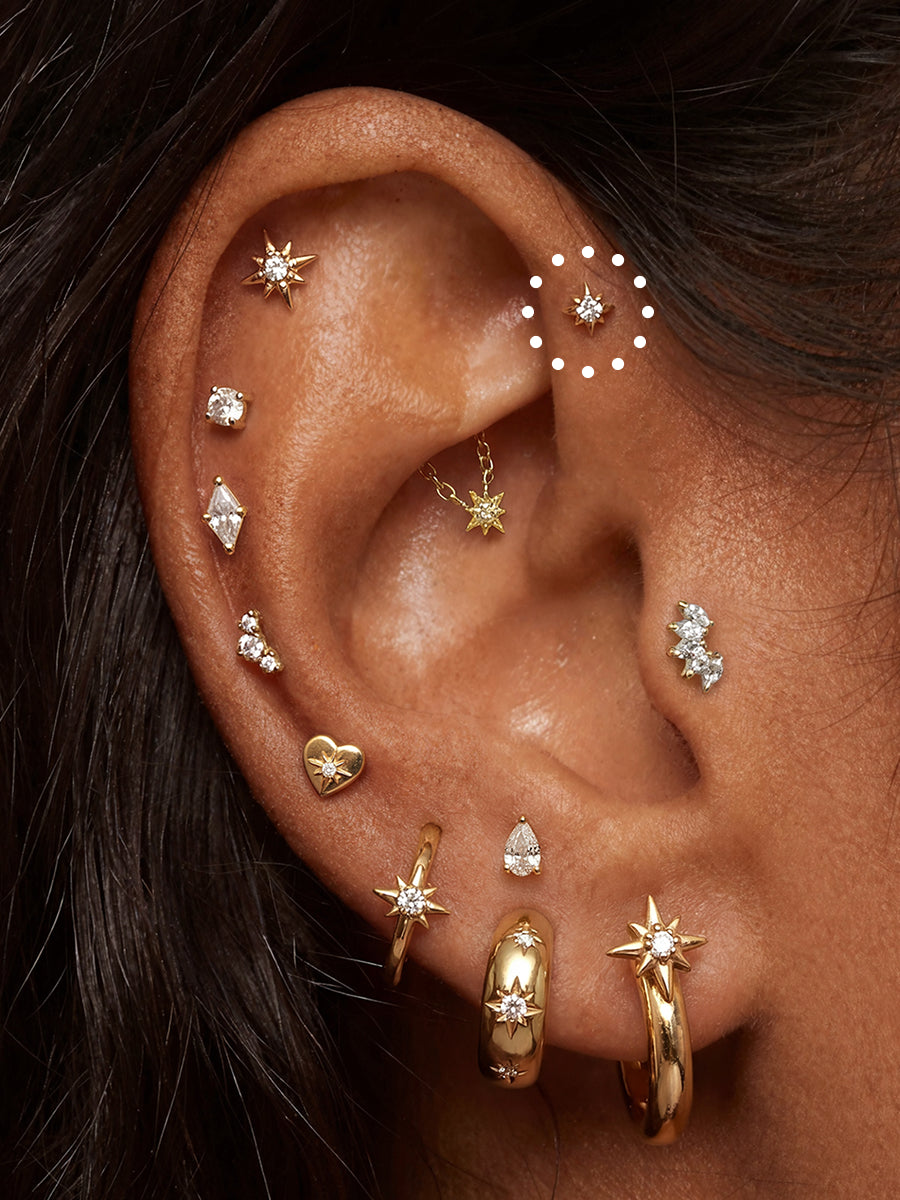 Close-up of a person's ear decorated with multiple gold and silver stud, hoop, and cartilage earrings, with a white dotted circle highlighting one of the ear cuff studs.