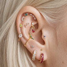 A close-up of a person's ear adorned with multiple jewel toned earrings from the new candy collection against a soft light background.