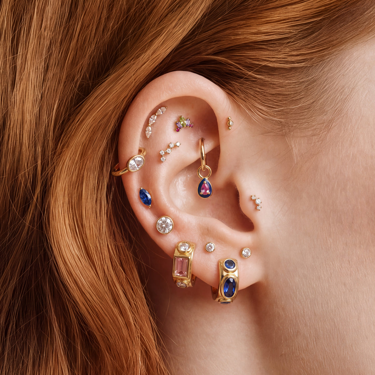 Close-up of a person's ear adorned with multiple gold ear piercings and earrings - featuring the STUDS Candy Collection