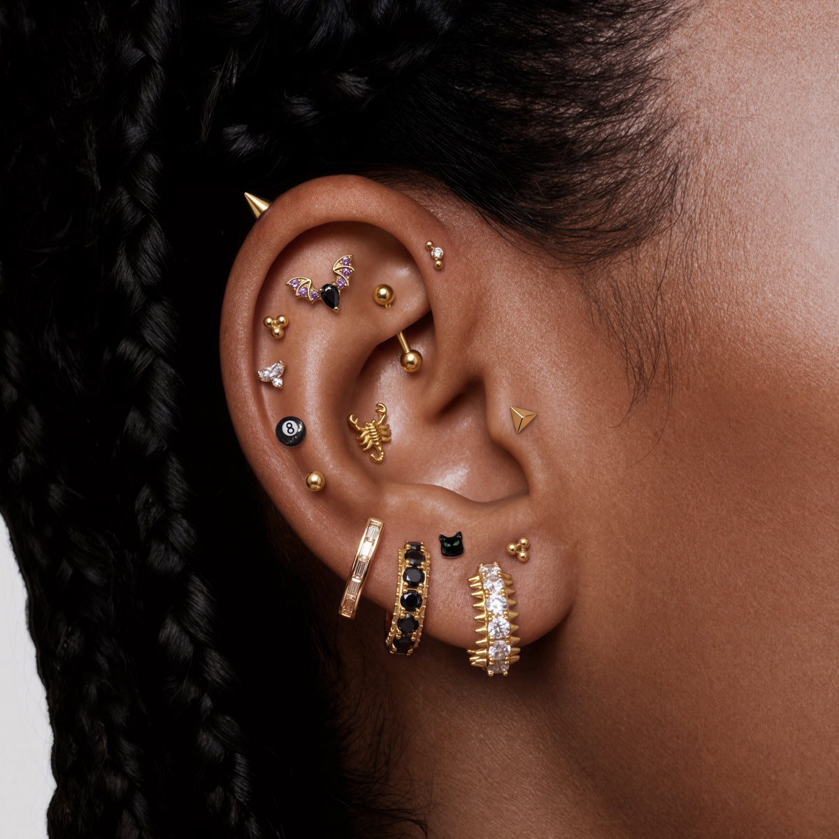 Close-up of a person's ear adorned with multiple gold and black pave earrings, featuring the new STUDS Halloween collection