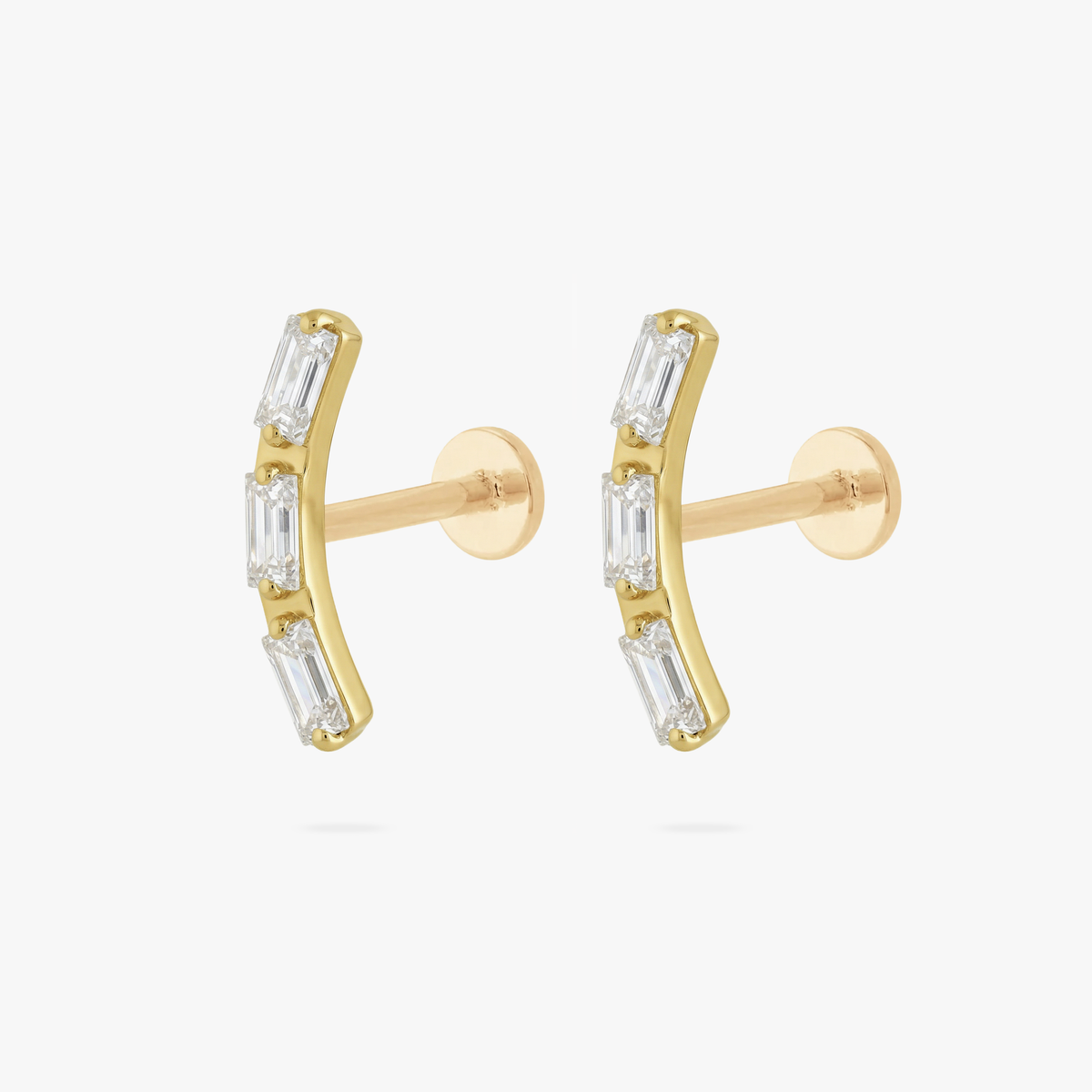 This is an image of a pair of gold toned flatback studs that are in the shape of two curved bars and each consist of three baguette cut, clear CZ stones.