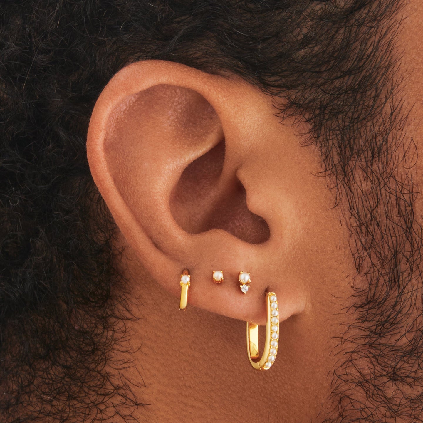 a set consisting of a pair of gold medium pearl oval hoops, a gold pearl helix huggie, a gold stacked cz pearl flatback stud, and a gold pearl stud on ear [hover] color:null|gold