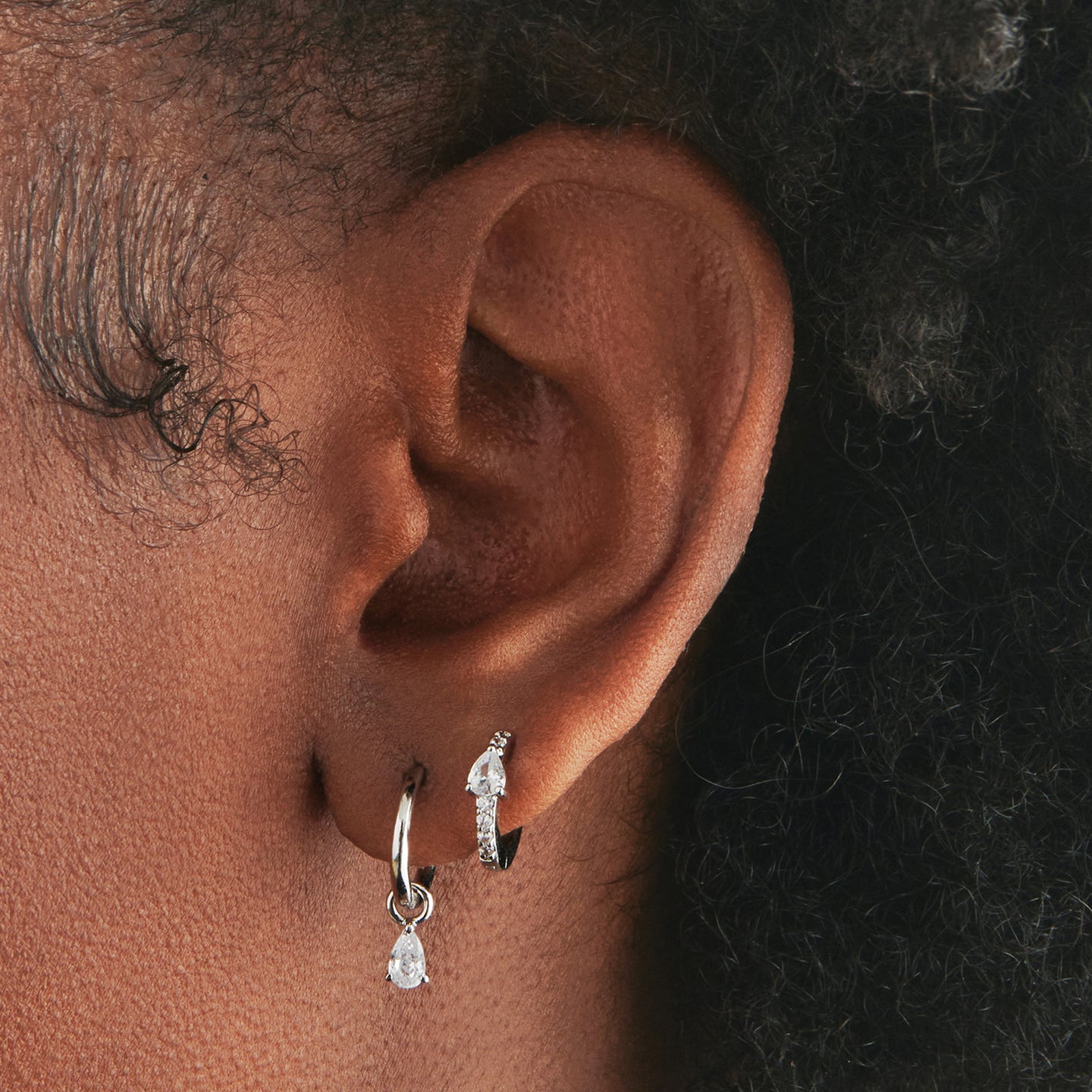 An image of a silver/clear mini pave huggie with a clear pear shaped CZ accent stone on ear. [hover] color:null|silver/clear
