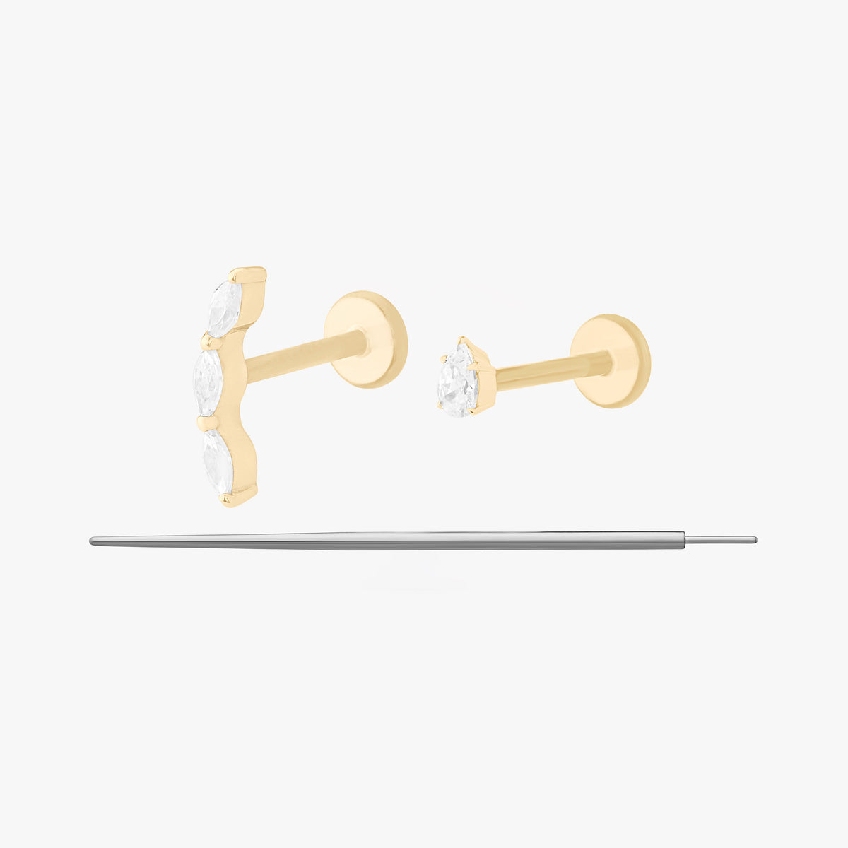 This image displays a set of two 14K gold flatback studs and a flatback insertion tool. The two earrings included in this set are the 14K Pear Clear Flatback Stud in gold/clear and 14K Curved CZ Pear Flatback Stud in gold/clear.