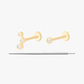 This image displays a set of two 14K gold flatback studs and a flatback insertion tool. The two earrings included in this set are the 14K Bezel Flatback Stud in gold/clear, as well as the 14K CZ Bezel Cluster Flatback Stud in gold/clear.