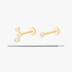 This image displays a set of two 14K gold flatback studs and a flatback insertion tool. The two earrings included in this set are the 14K Bezel Flatback Stud in gold/clear, as well as the 14K CZ Bezel Cluster Flatback Stud in gold/clear.