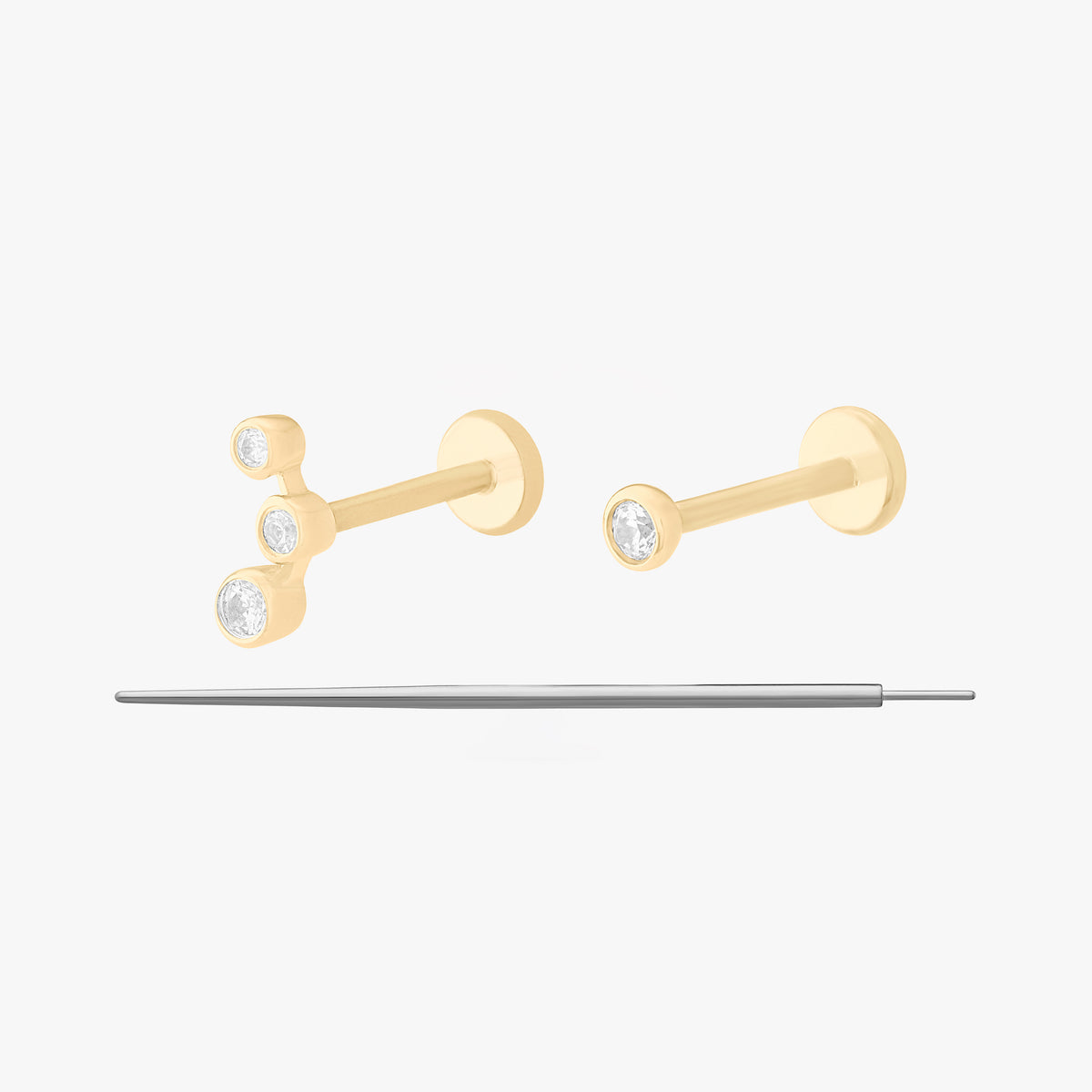 This image displays a set of two 14K gold flatback studs and a flatback insertion tool. The two earrings included in this set are the 14K Bezel Flatback Stud in gold/clear, as well as the 14K CZ Bezel Cluster Flatback Stud in gold/clear.