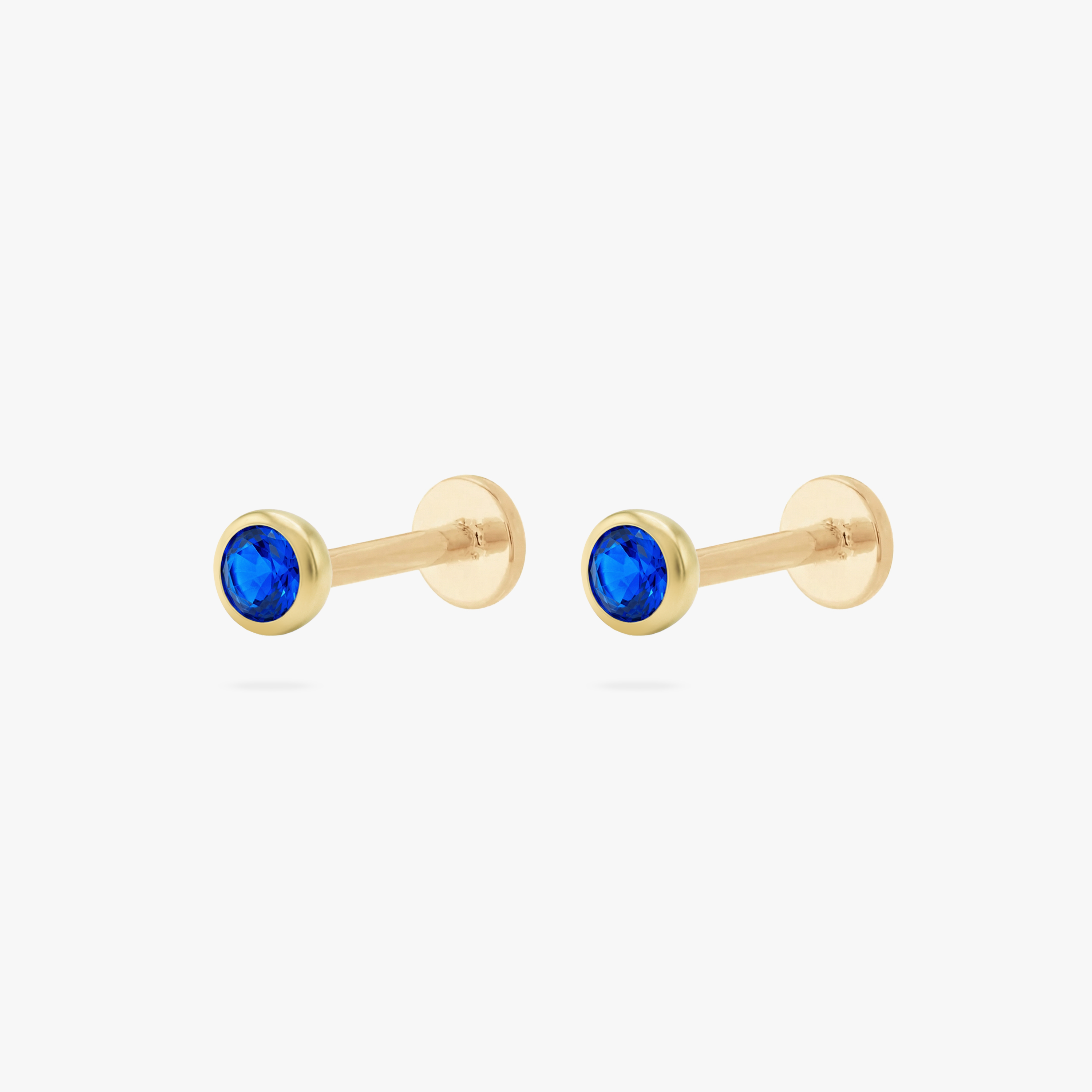 This is an image of a pair of gold toned flatback studs with 3mm, bezel set blue CZ stones. - Pair view