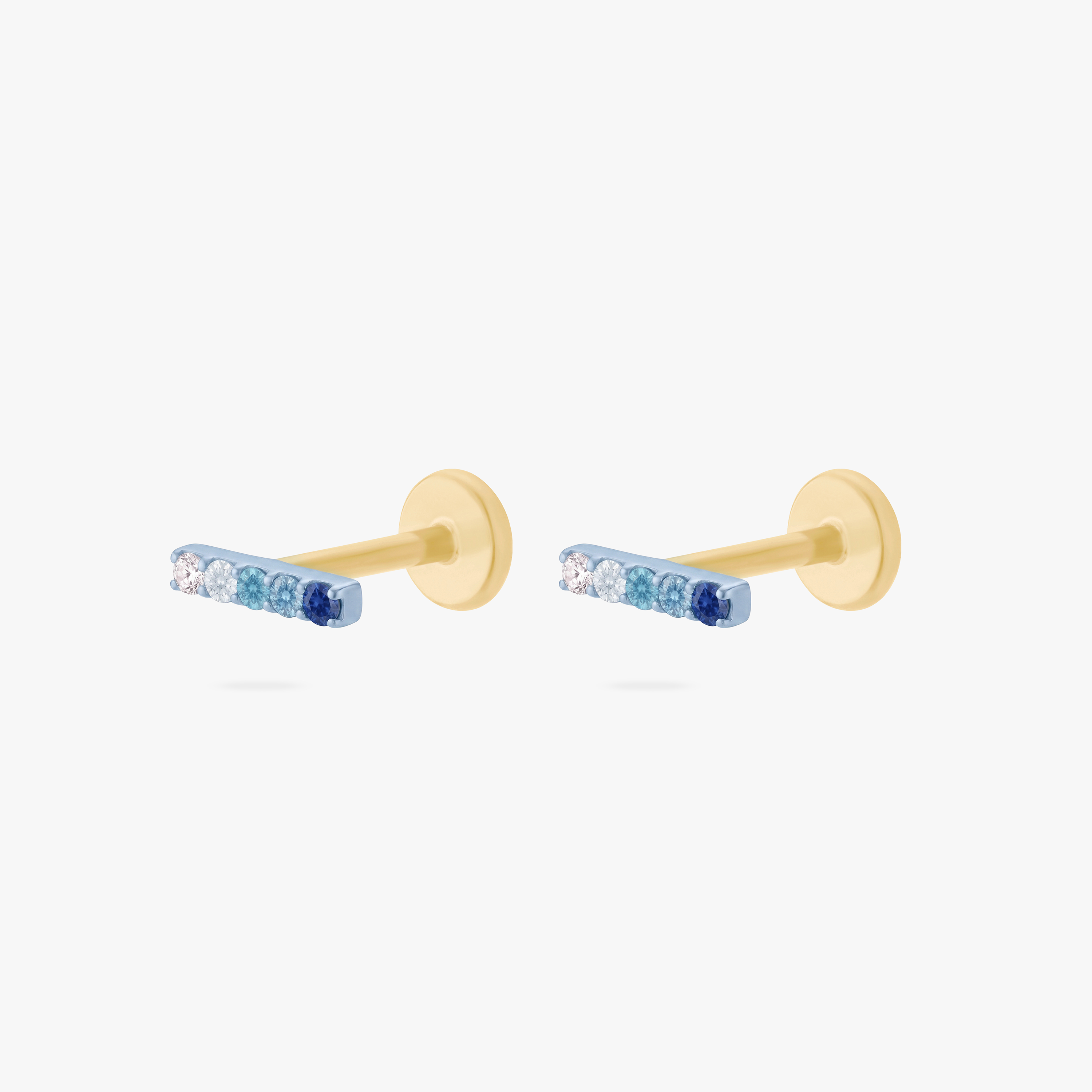 This is an image of a pair of anodized blue flatback studs each displaying a gradient of 5 blue CZ stones creating a pave bar. The flatback post for these earrings are gold toned. - Pair view