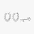 This image shows a set of silver earrings.  The set includes a pair of silver french twist huggies and a singular bow flatback stud. 