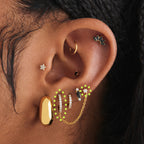 This image shows an earscape featuring a gold plated pave huggie conected to a stud by a connector chain with clear cz stones