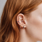This image shows an earscape featuring the Anodized Stone Crown Flatback. The flatback has a green pear cz stone in the middle, two purple cz baguette stones on either side and two pink circular cz stones on the outer side of the baguette stones. 
