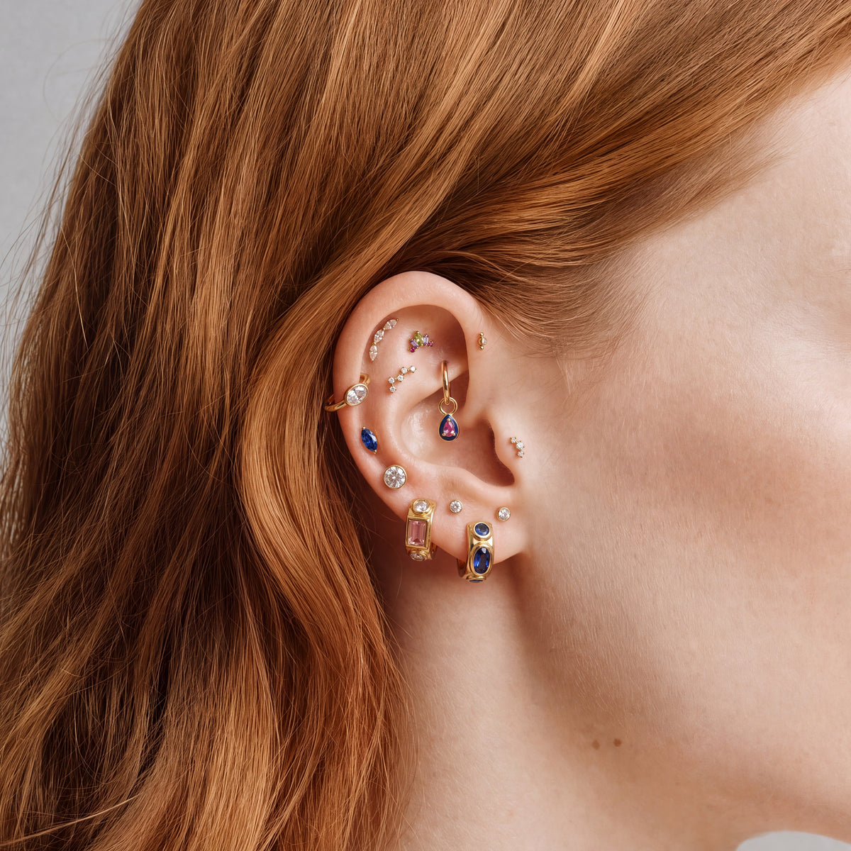 This image shows an earscape featuring the Anodized Stone Crown Flatback. The flatback has a green pear cz stone in the middle, two purple cz baguette stones on either side and two pink circular cz stones on the outer side of the baguette stones. 