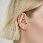 This image show an earscape featuring the anodized triangle crown flatback. the flatback has a blue cz stone on the top, a pear red cz stone on the bottom and four  pink cz circular stones on each side of the earring. 