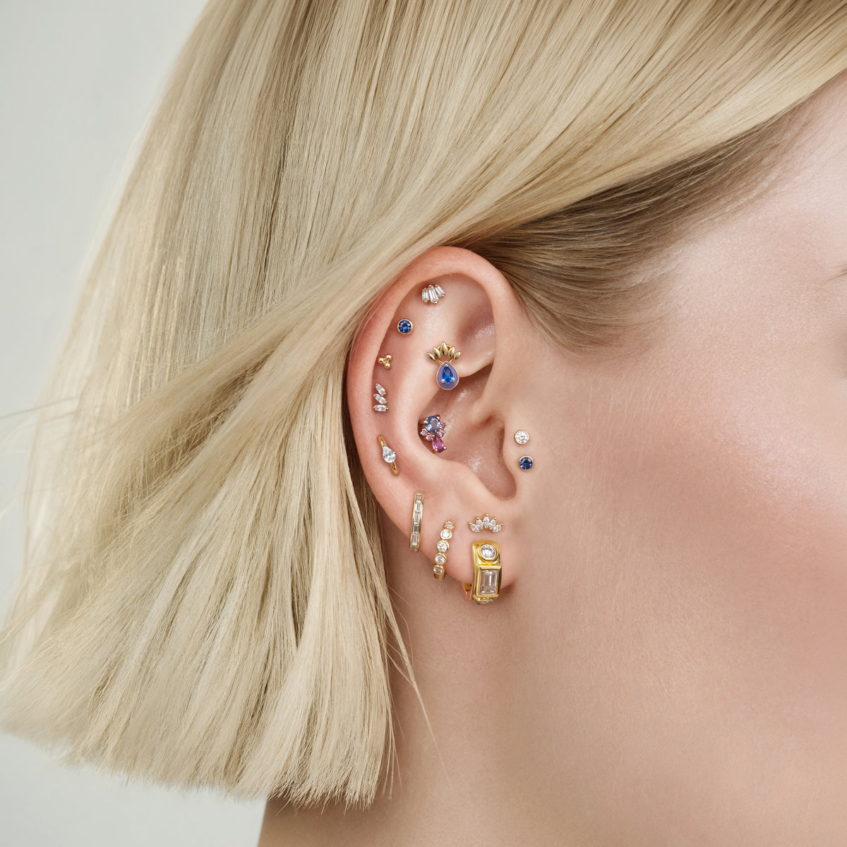 This image show an earscape featuring the anodized triangle crown flatback. the flatback has a blue cz stone on the top, a pear red cz stone on the bottom and four  pink cz circular stones on each side of the earring. 