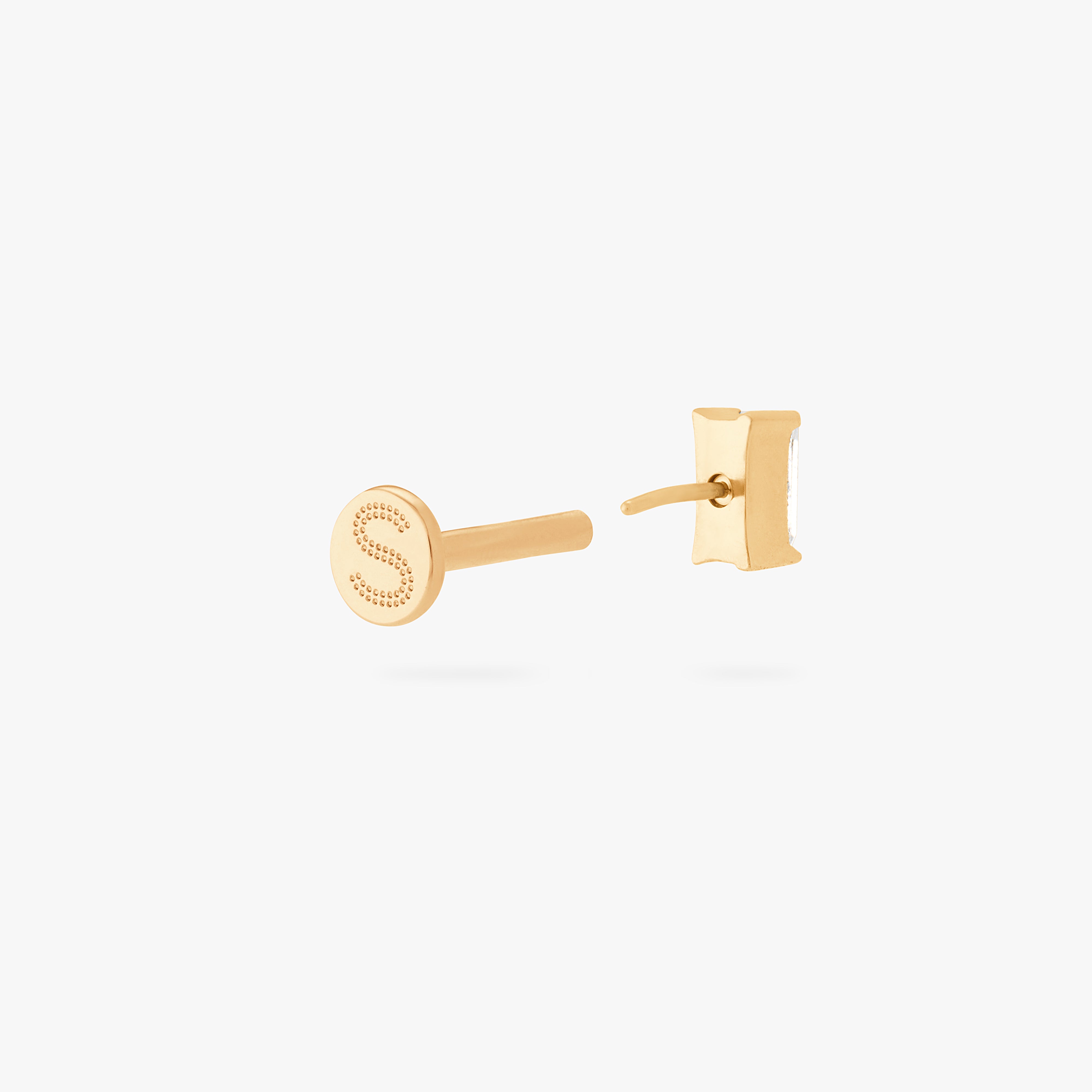 This is an image of a gold/clear baguette shaped CZ flatback stud, with a gold labret with a circle disc with an "S" logo engraved on it. color:null|gold/clear