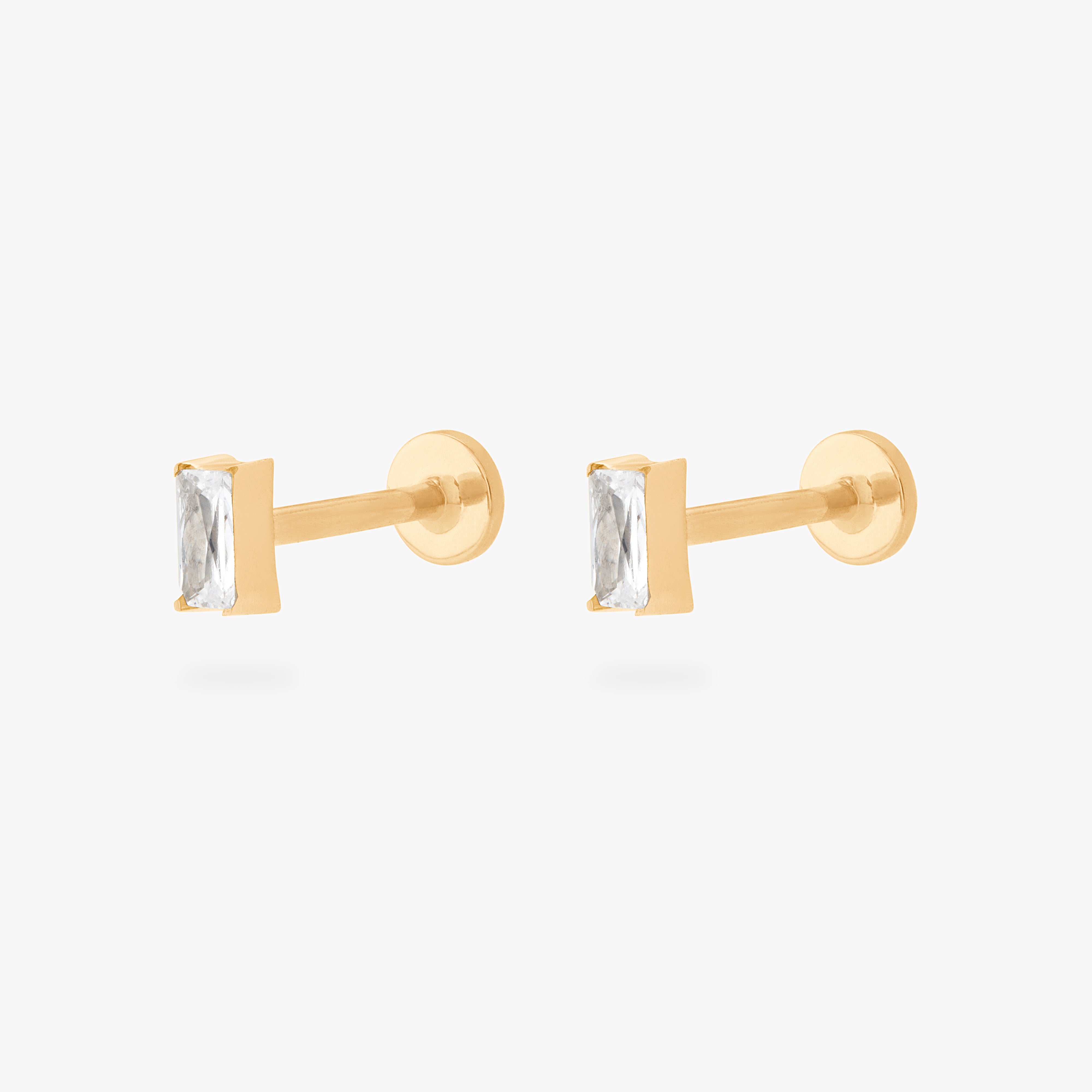 This is an image of a pair of gold/clear baguette shaped CZ flatback studs, with gold labrets with circle discs with "S" logos engraved on them. [pair] color:null|gold/clear