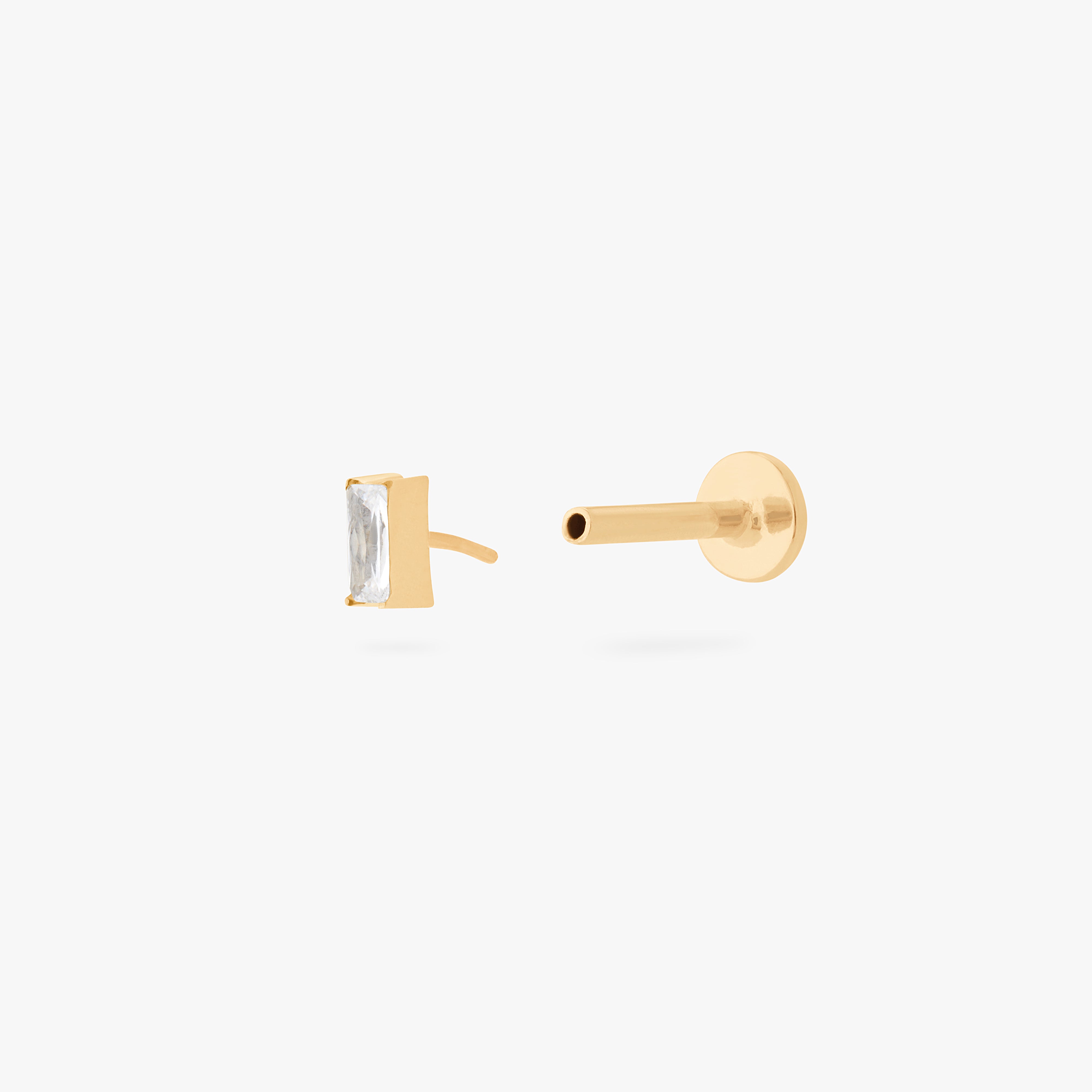 This is an image of a gold/clear baguette shaped CZ flatback stud, with a gold labret with a circle disc with an "S" logo engraved on it. color:null|gold/clear