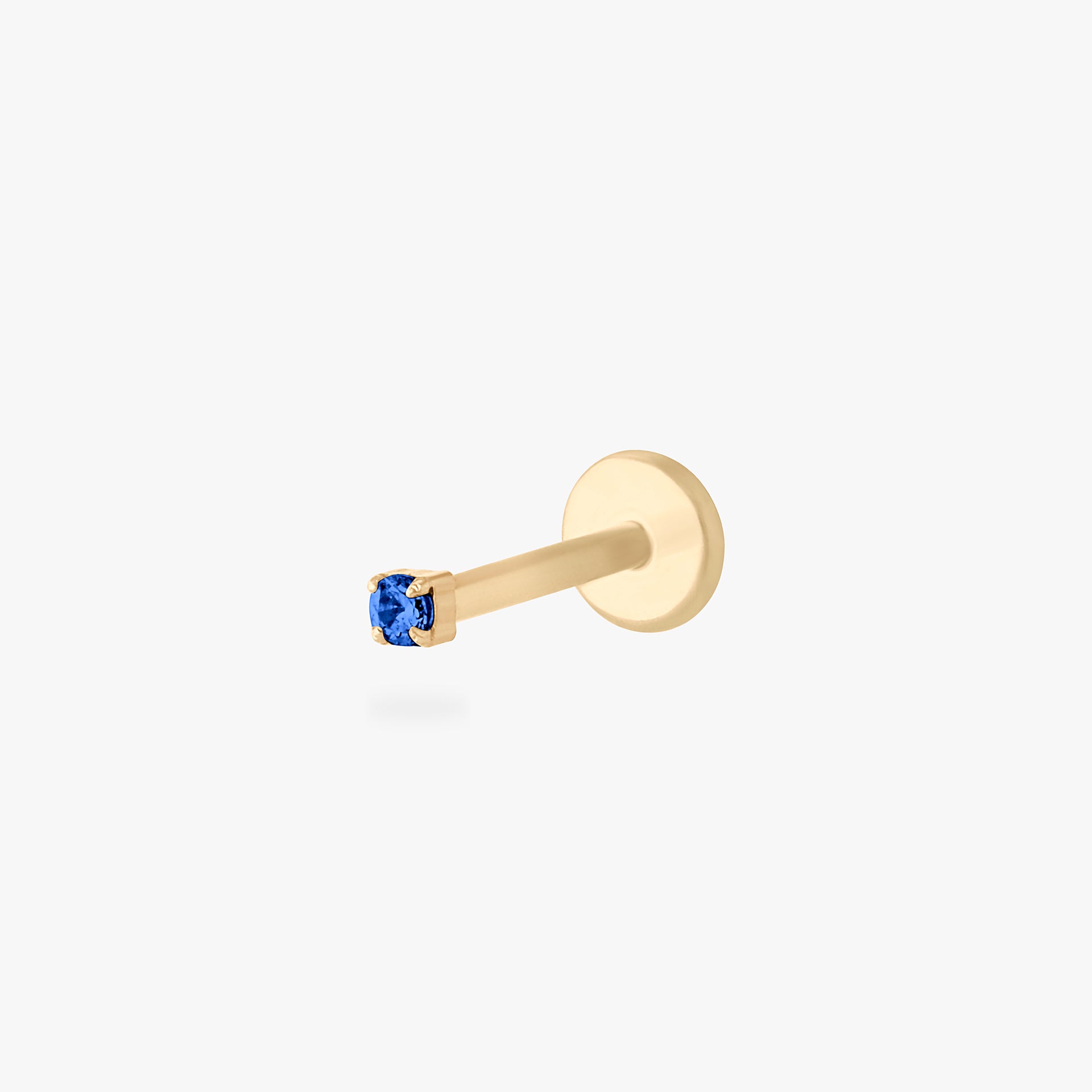 This is an image of a gold toned titanium flatback stud with a micro sized sapphire CZ stone against a white background. - Main view