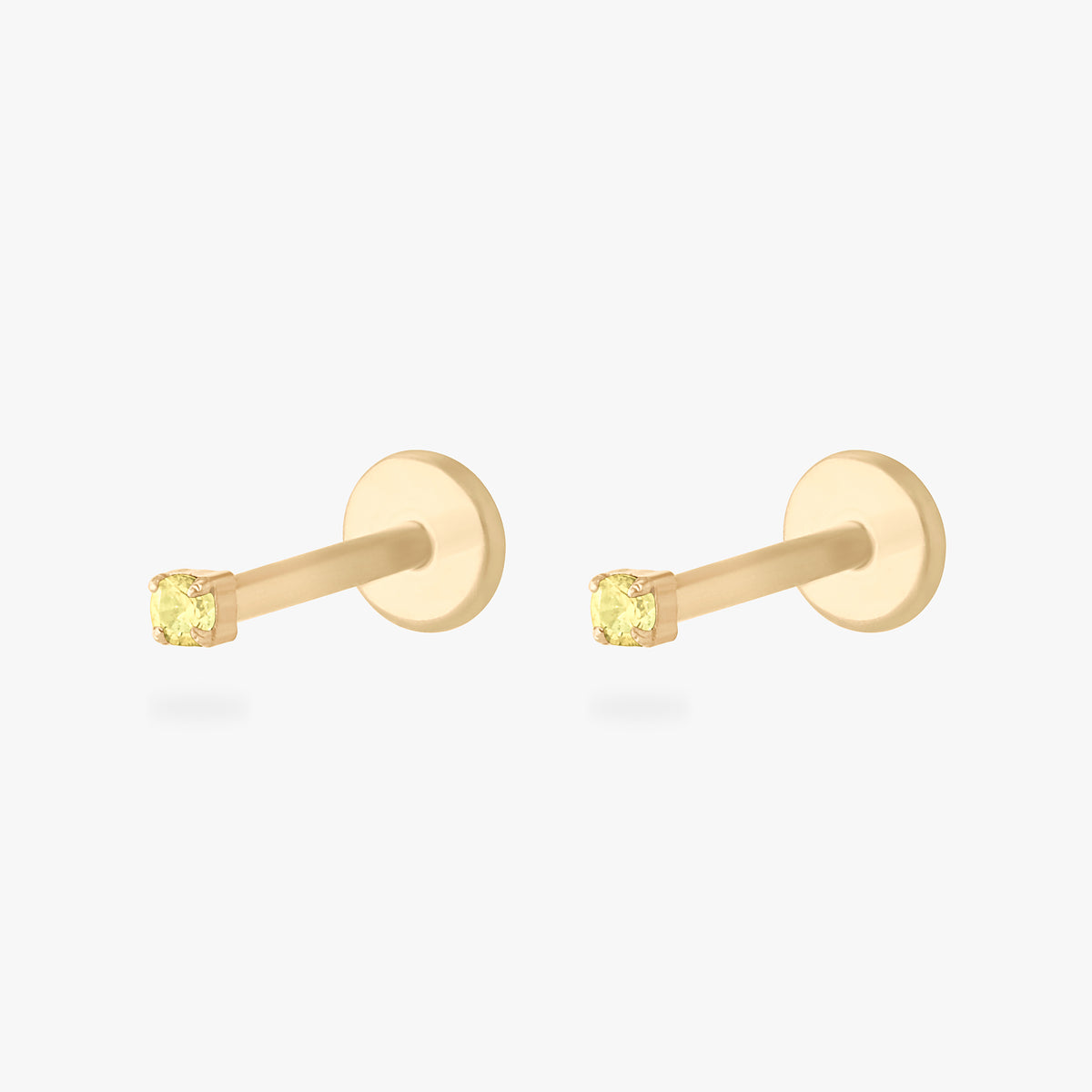 Pair of gold micro CZ flatback stud earrings with small yellow stones in prong setting displayed side by side