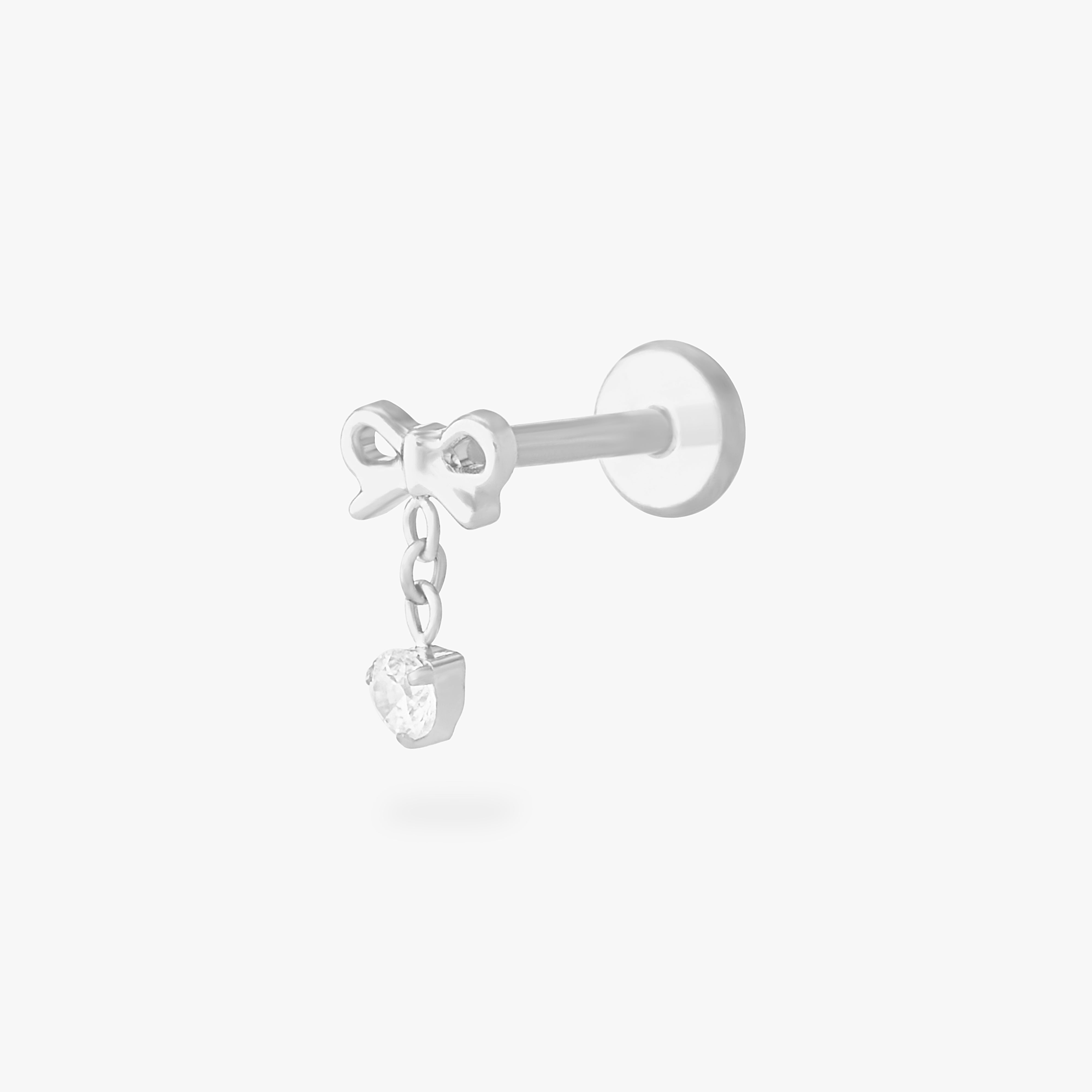 This is an image of a silver-toned flatback stud with a bow that a chain with a CZ dangles from. color:null|silver/clear