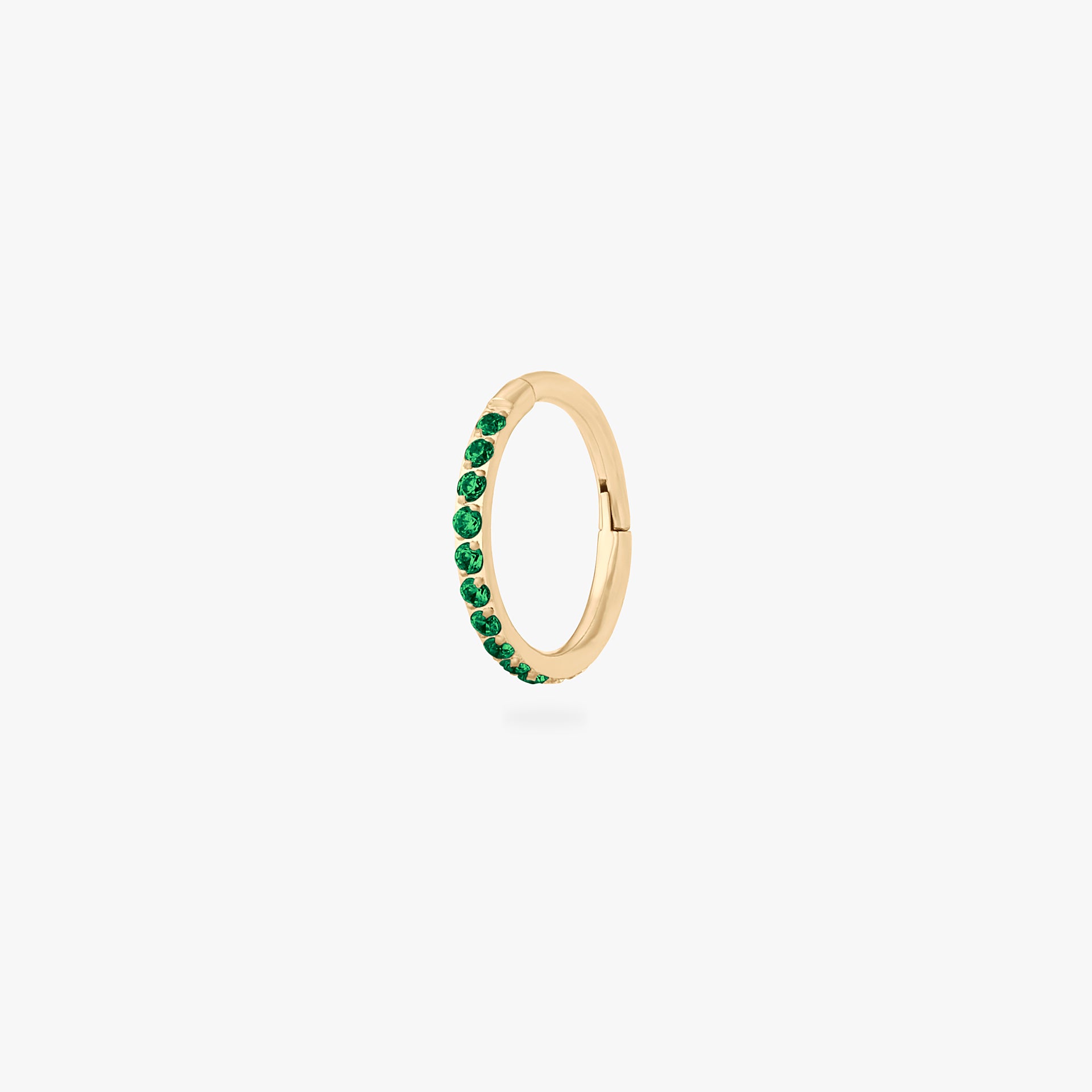 This is an image of a gold toned titanium clicker with an 8mm diameter and green cz stones in a pave setting. - Main view