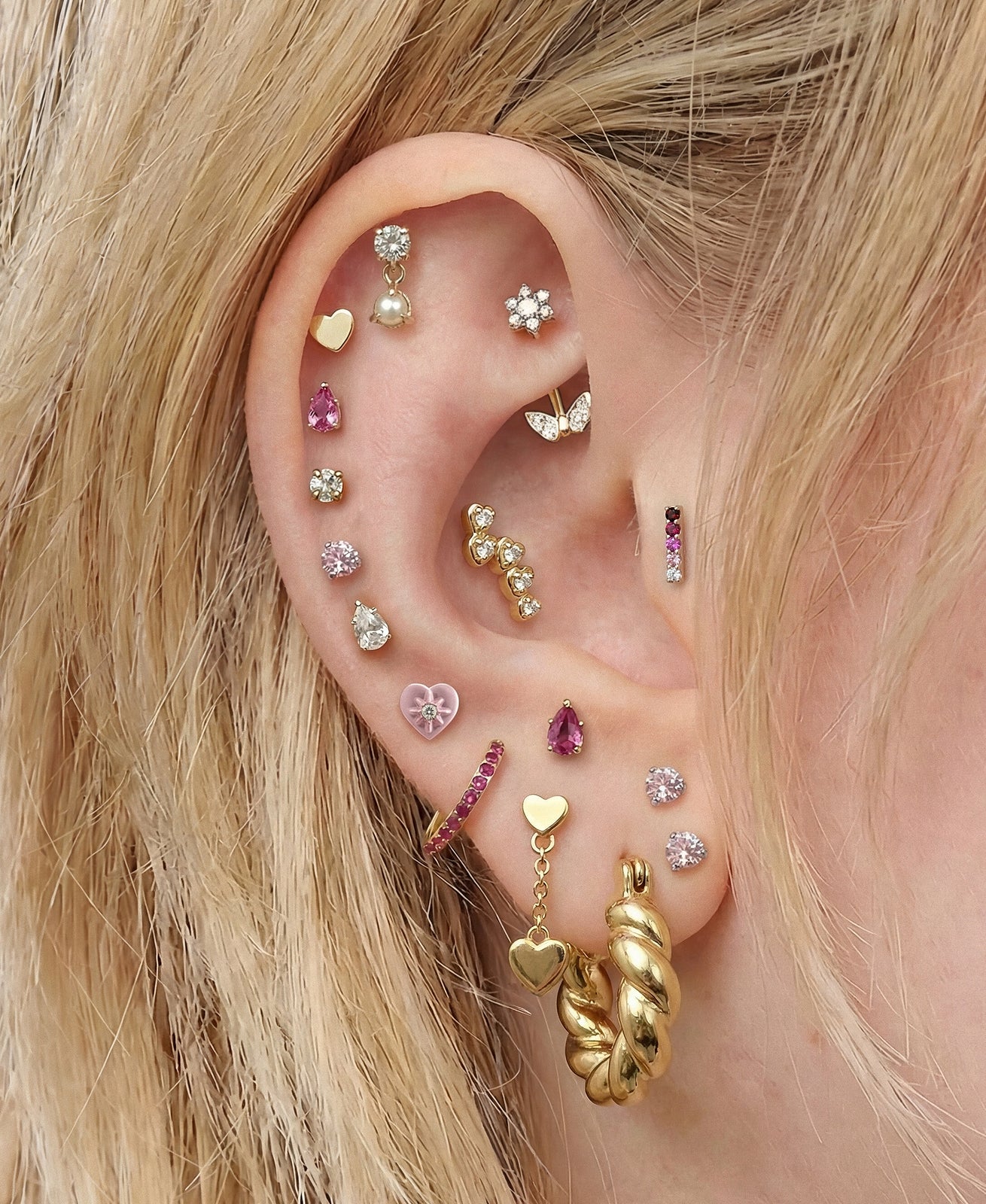 Close-up of an ear with multiple earrings including gold, pink, and heart-shaped designs.