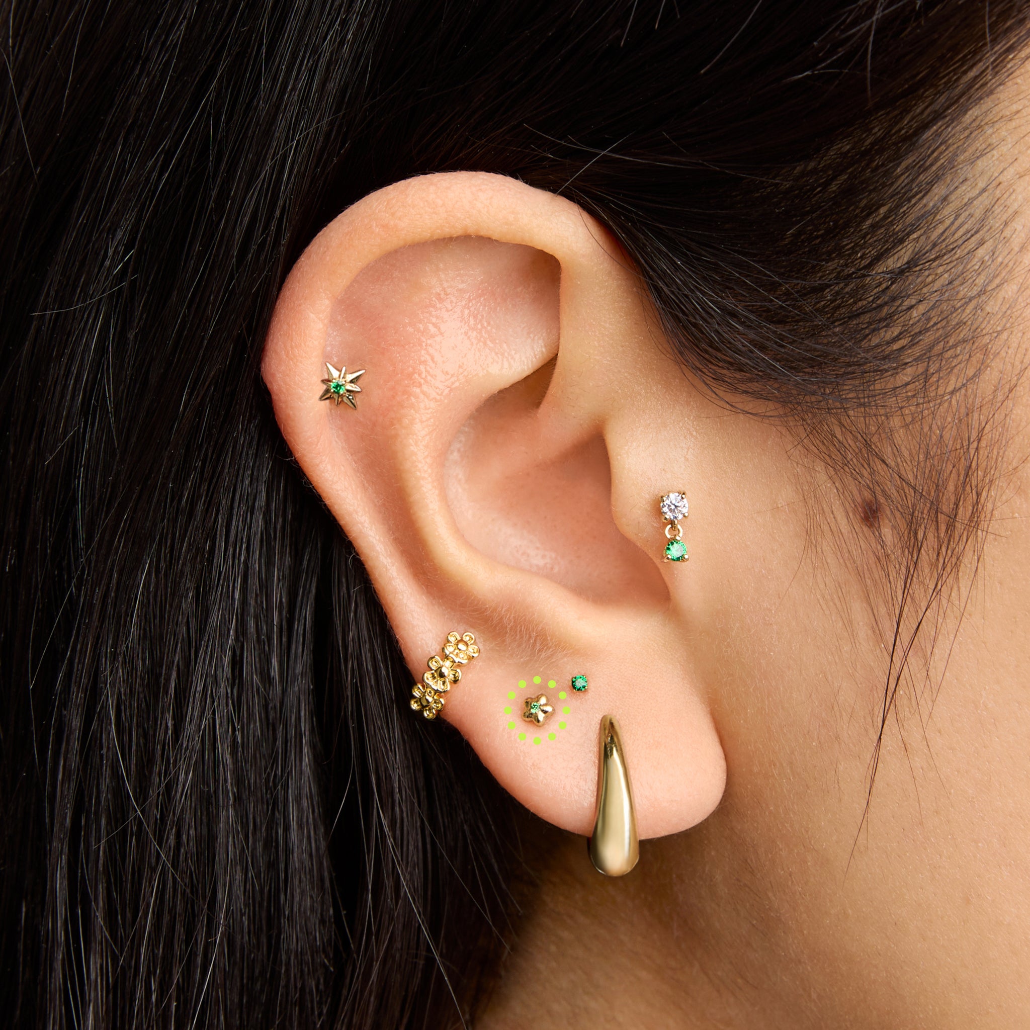 This is an image of a gold toned flatback stud that is shaped like a flower with a green cz in the center on ear. [hover] color:null|gold/green