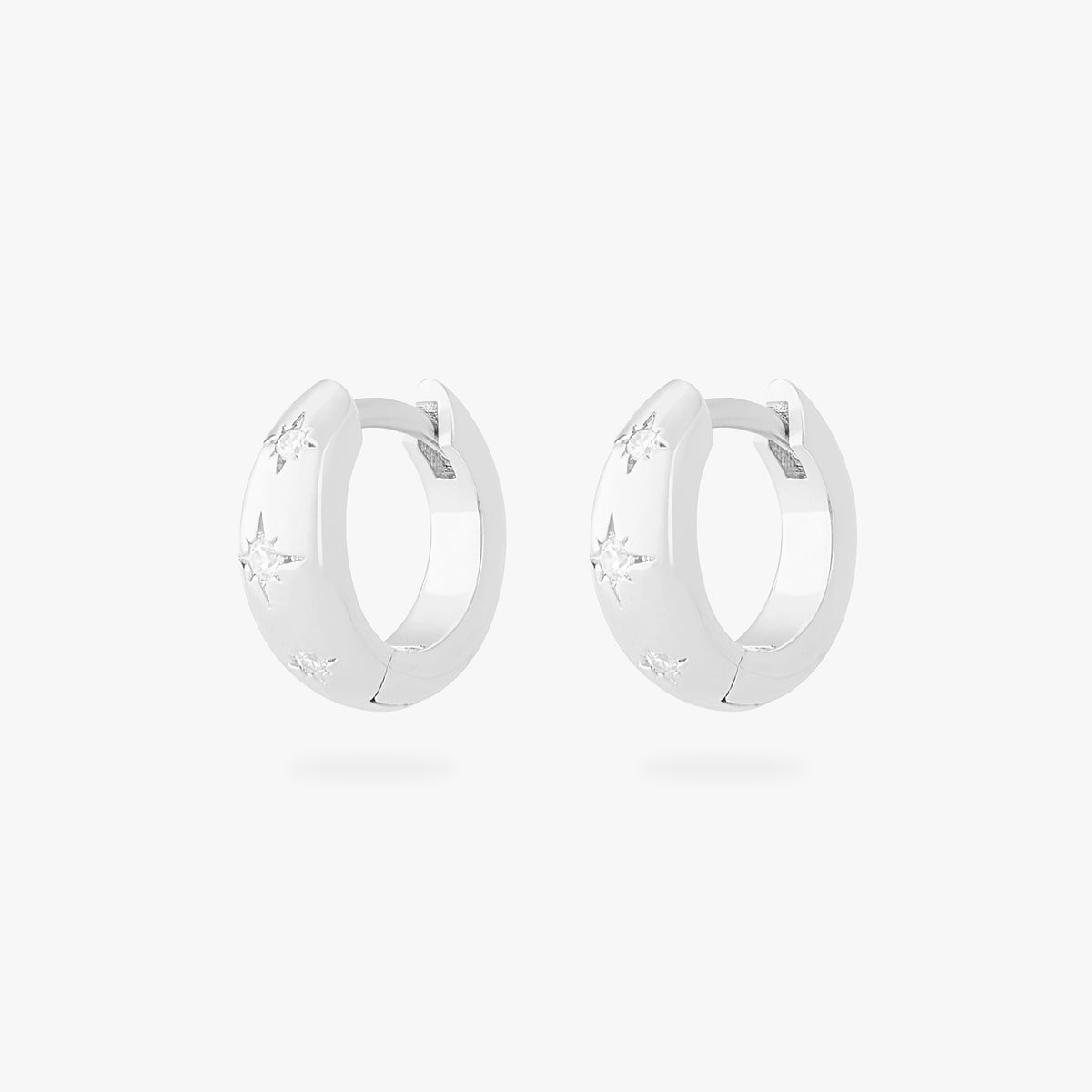 This is an image of a pair of silver-toned huggies with twinkle star shaped engravings with CZs in them. [pair] color:null|silver/clear