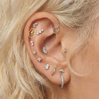 Close-up of an ear with multiple silver sparkly earrings with a micro cluster flatback circled in the helix