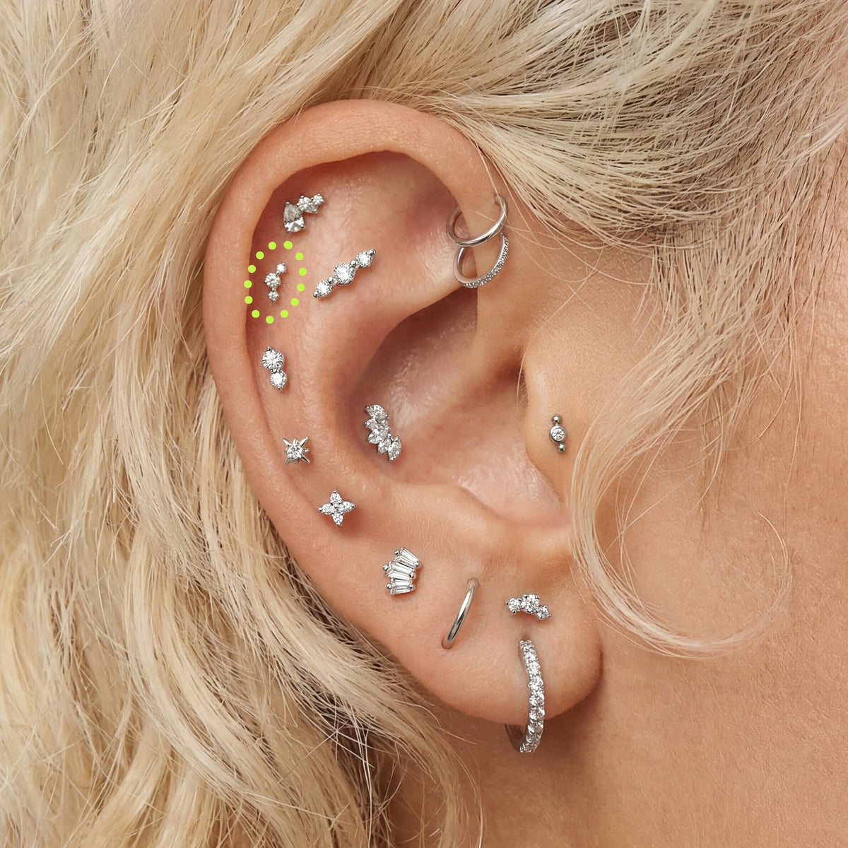 Close-up of an ear with multiple silver sparkly earrings with a micro cluster flatback circled in the helix