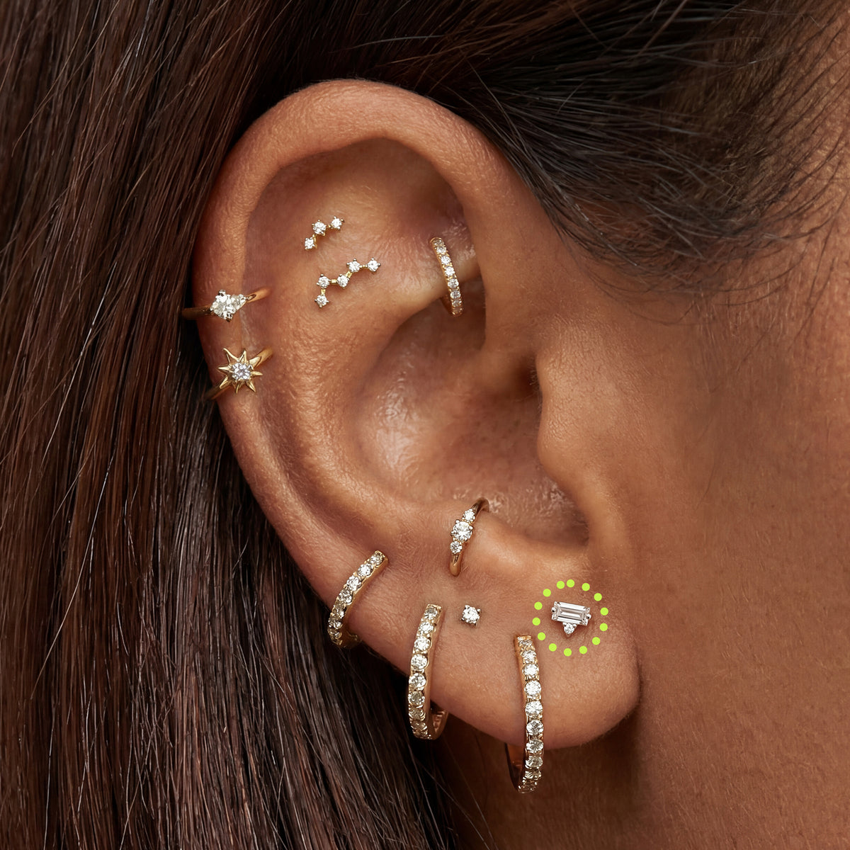 Close-up of an ear with multiple sparkly gold earrings with a micro stacked baguette flatback circled in the stacked lobe