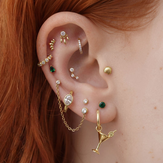 this image shows an ear with a 14k gold plated huggie with a martini charm and a  gemstone 
