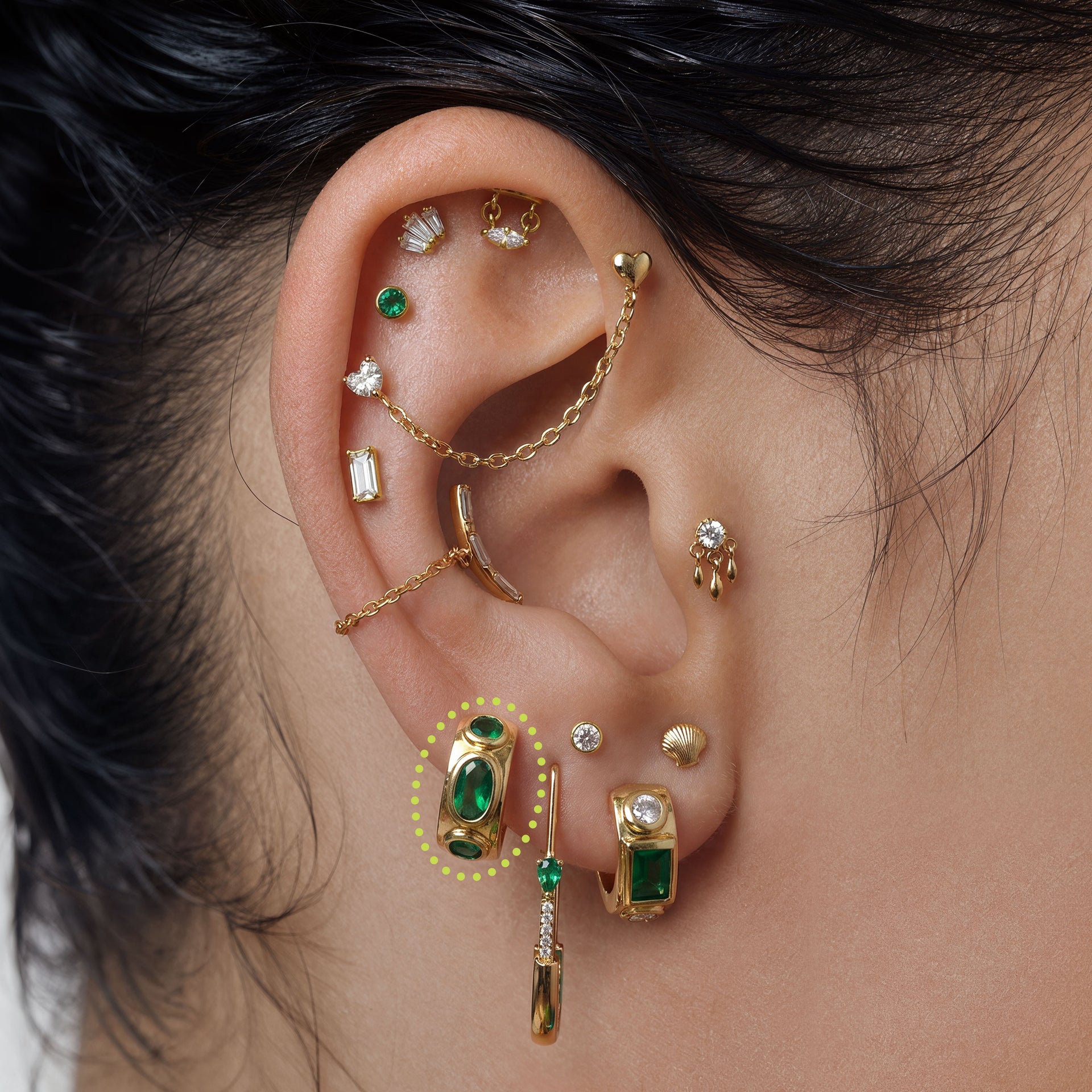 this image shows an ear with a 14k gold plated huggie with three green circular cz stones - Alternative view 1